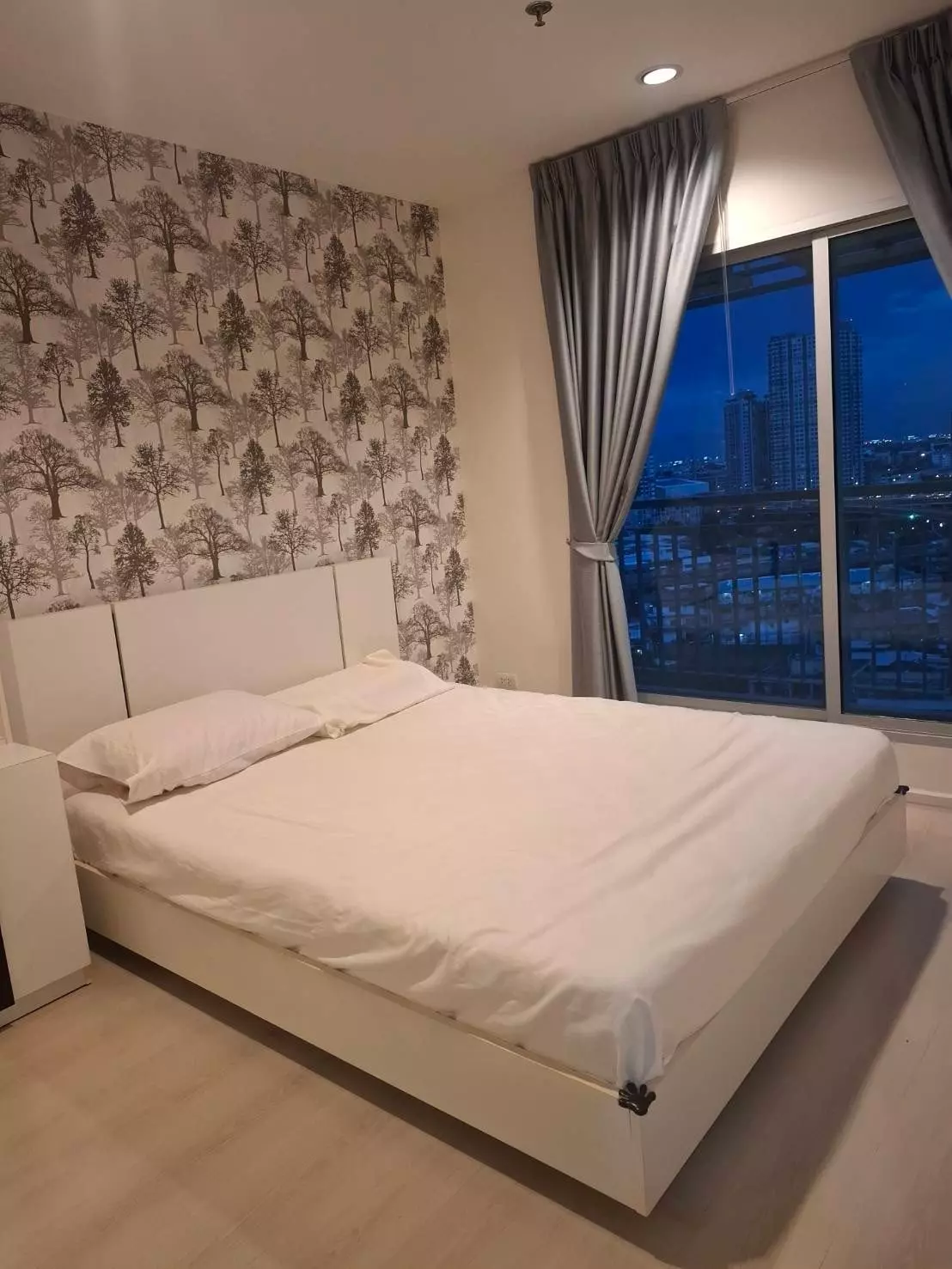 Queen bedroom in Aspire Sukhumvit 48 condo featuring a tree-patterned feature wall and floor-to-ceiling city night views