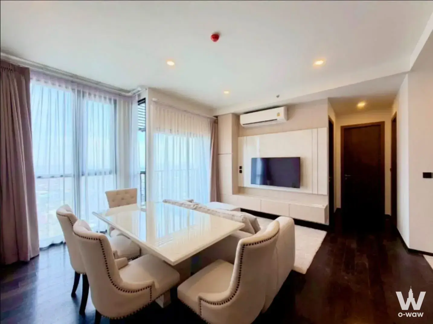 Dining area in a Noble BE19 condo with a white table, cream chairs, and a wall-mounted TV on dark wood floors