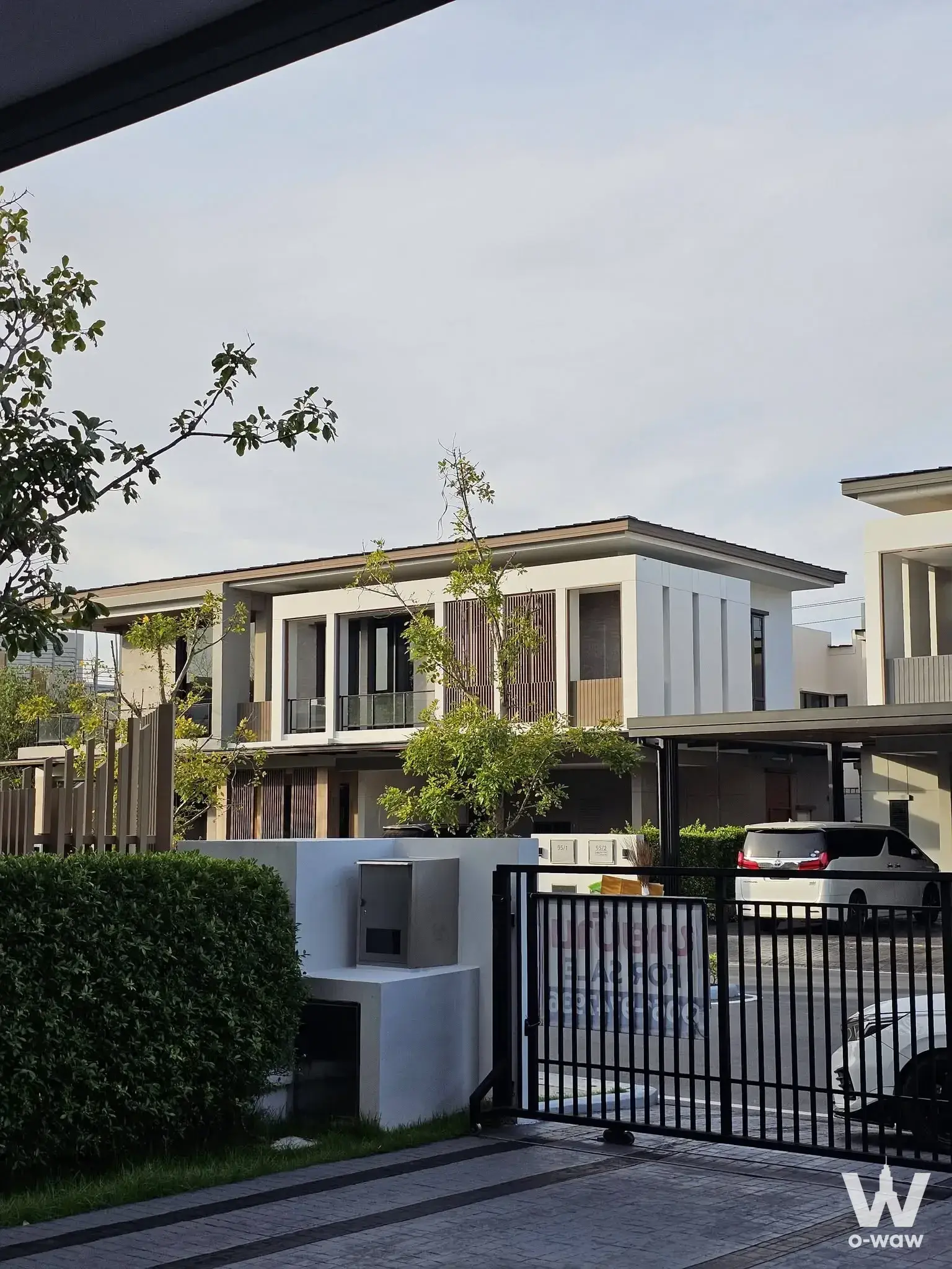 Exterior of a Bangkok Boulevard townhouse for sale showing white walls, wood slats, and carport