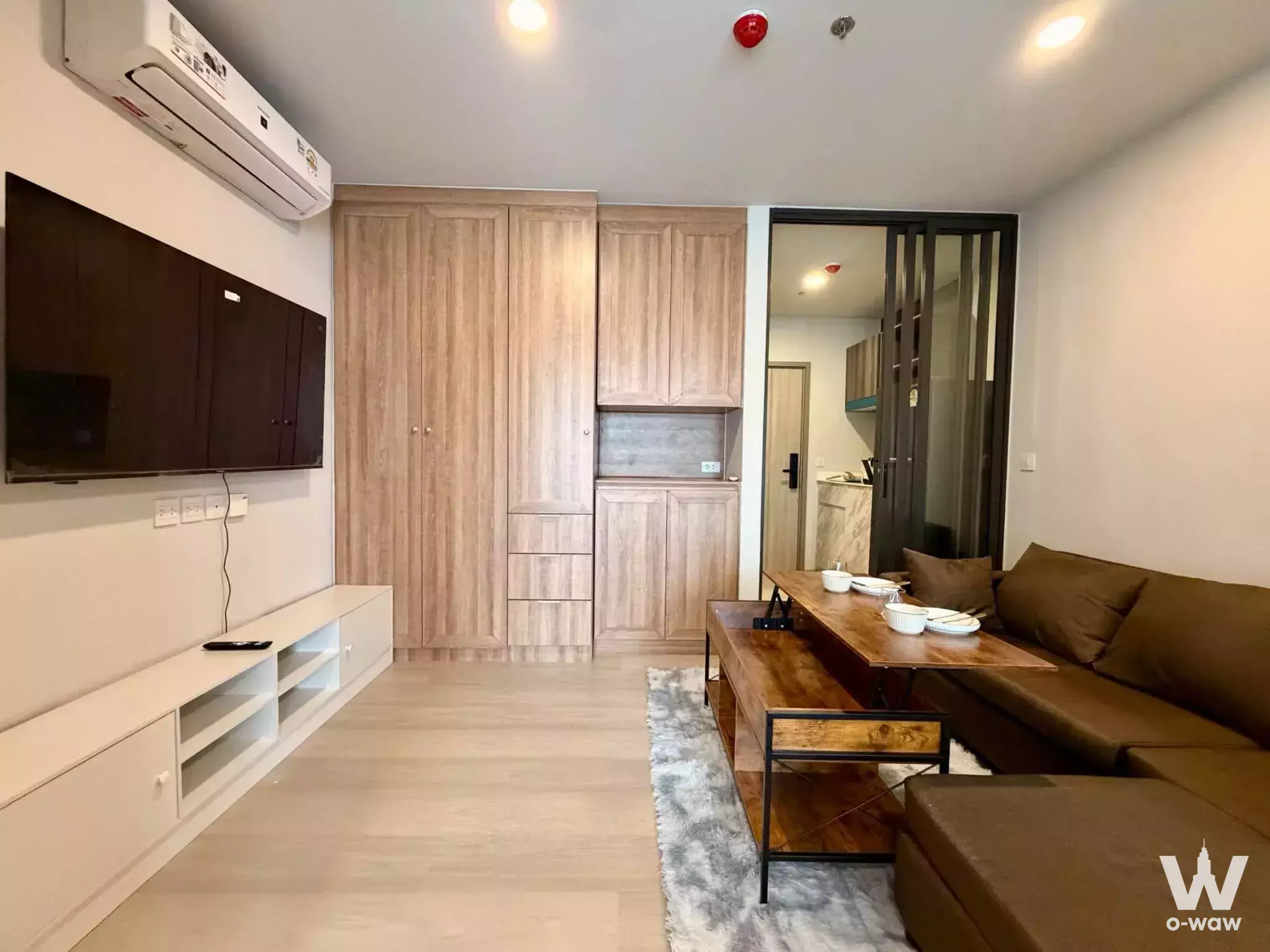 Living room in Aspire Onnut Station 1-bed condo featuring a black TV wall and light wood cabinetry