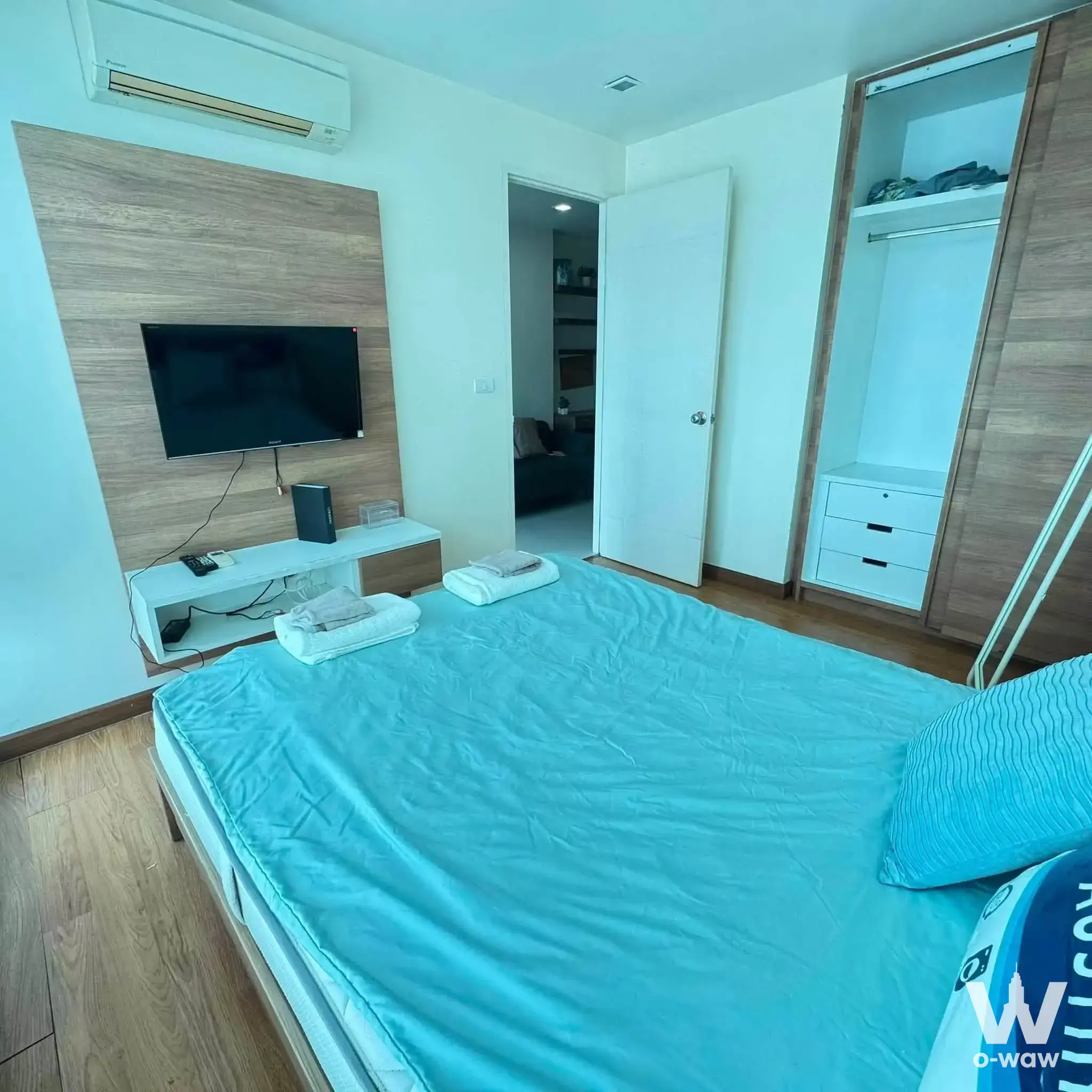 Bright bedroom in a 1-bed condo for rent at Wish@SamYan, featuring a cyan duvet and wood-grain accent wall