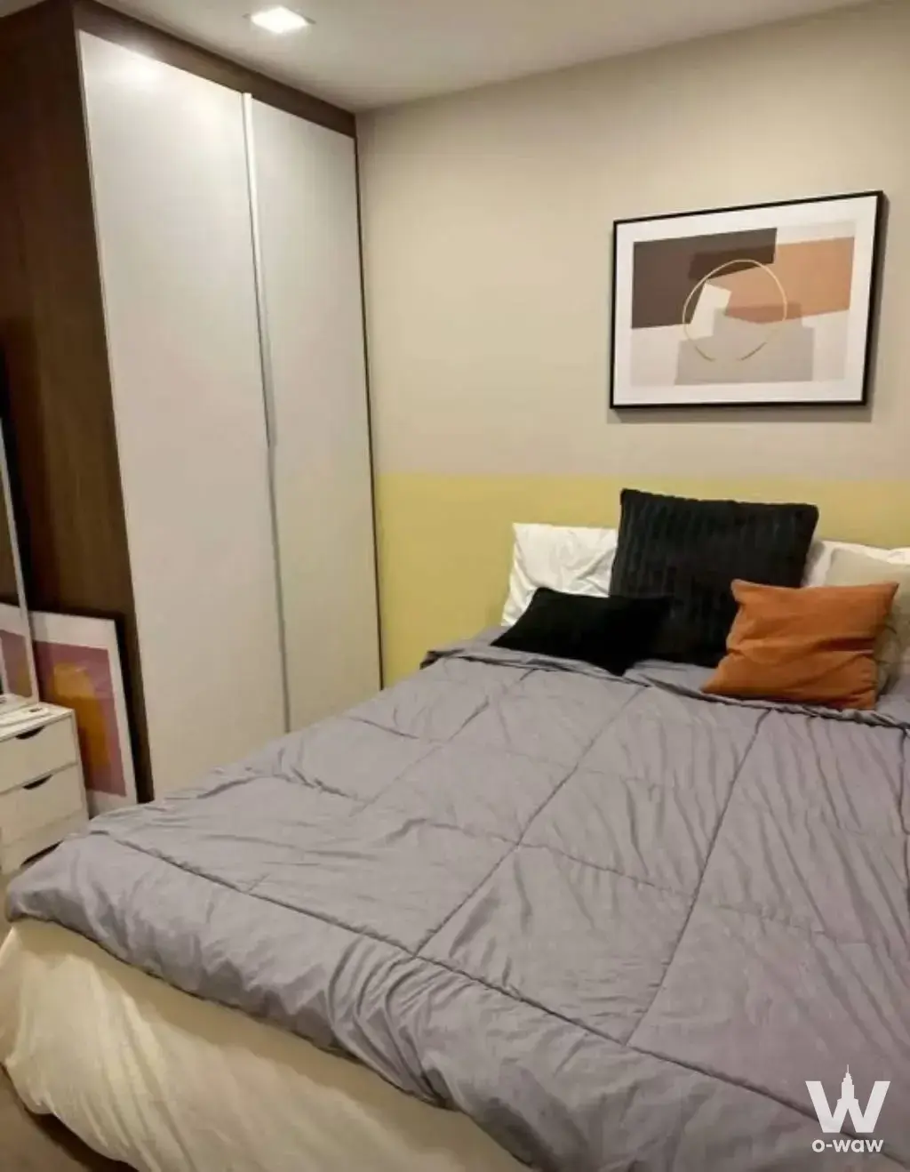 This Atmoz Ladprao 71 2-bed condo for rent has a bedroom with a grey quilted bed and a yellow accent wall