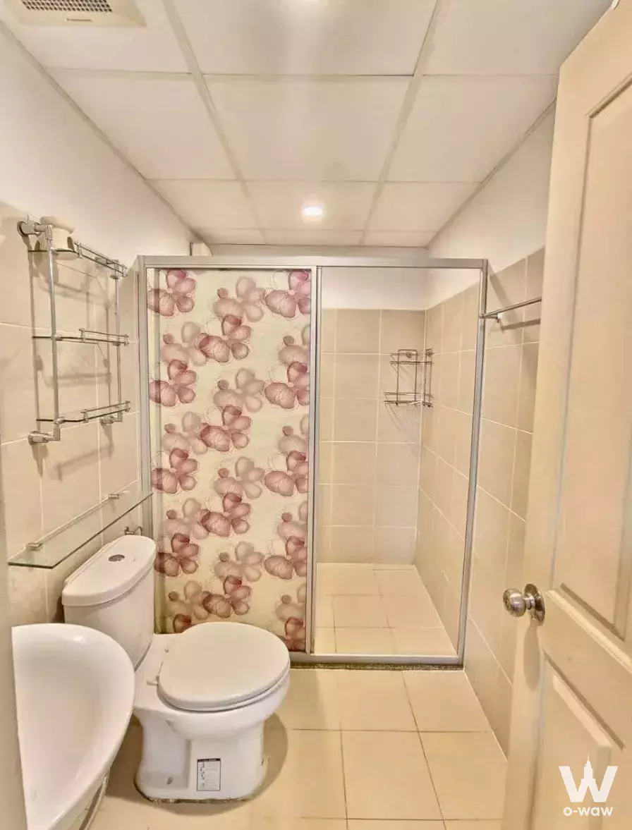 Compact bathroom in a Supalai Park Khaerai-Ngamwongwan condo featuring cream tiles and a floral shower curtain