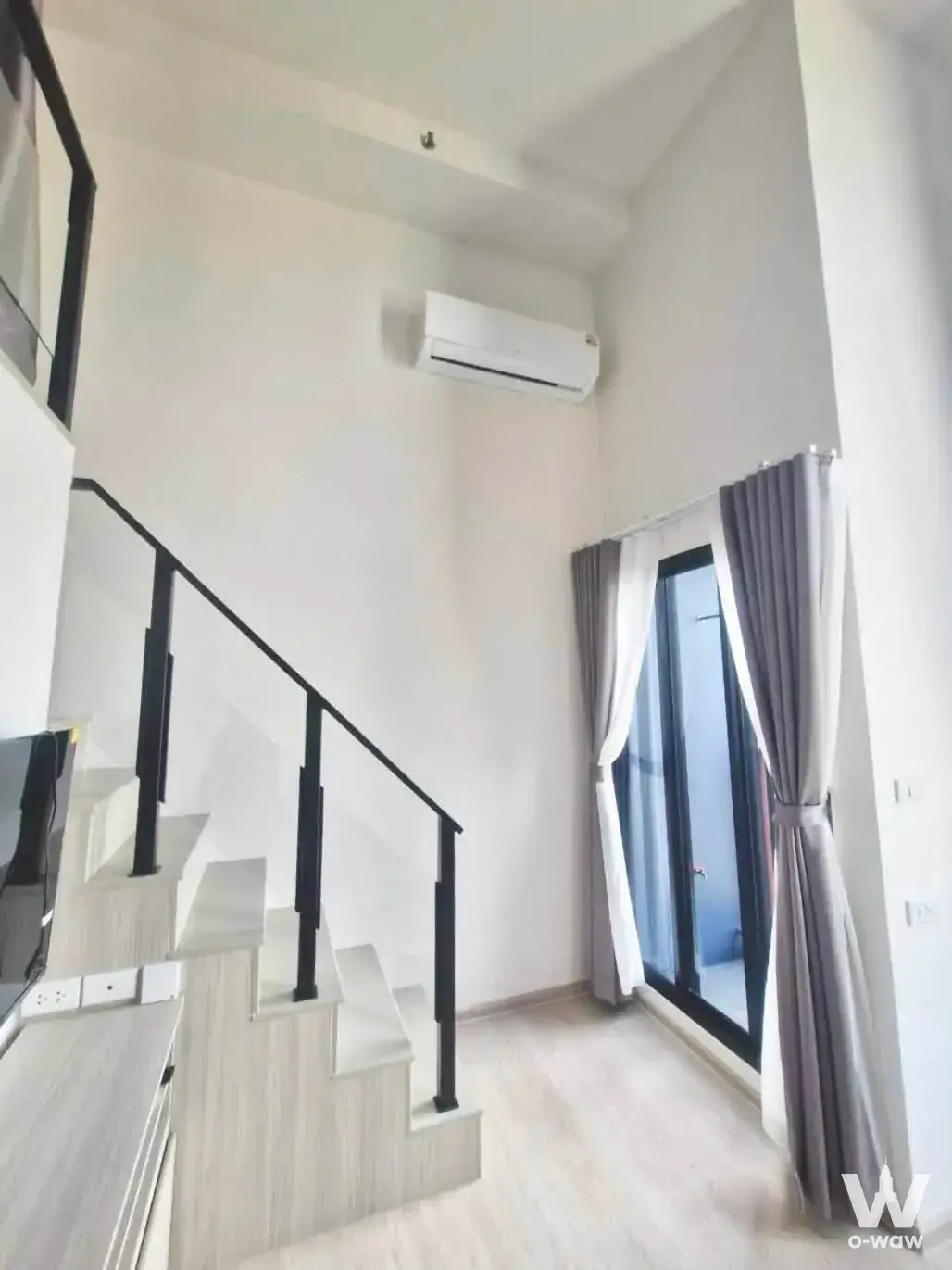 Interior stairwell with light wood steps and black railings leading to a glass door balcony in a 1-bed condo for rent at