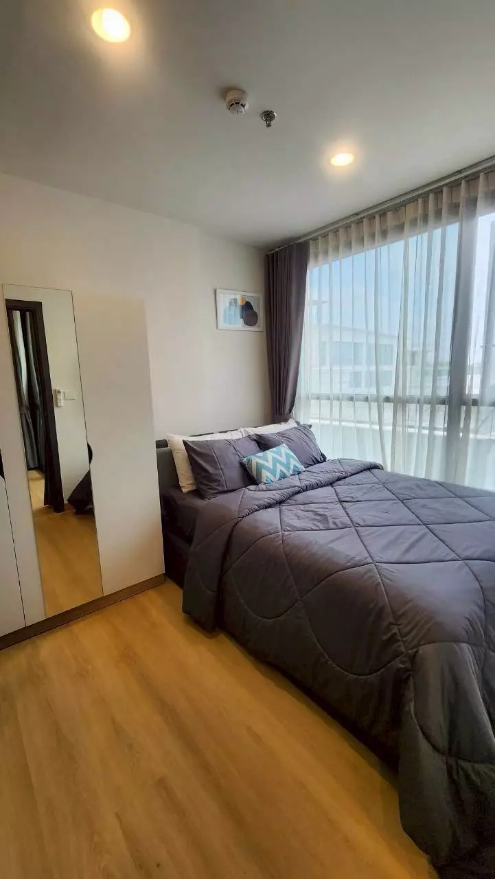 Bedroom in XT Huaikhwang condo with queen bed, teal accent pillow, and sheer curtains on floor-to-ceiling window