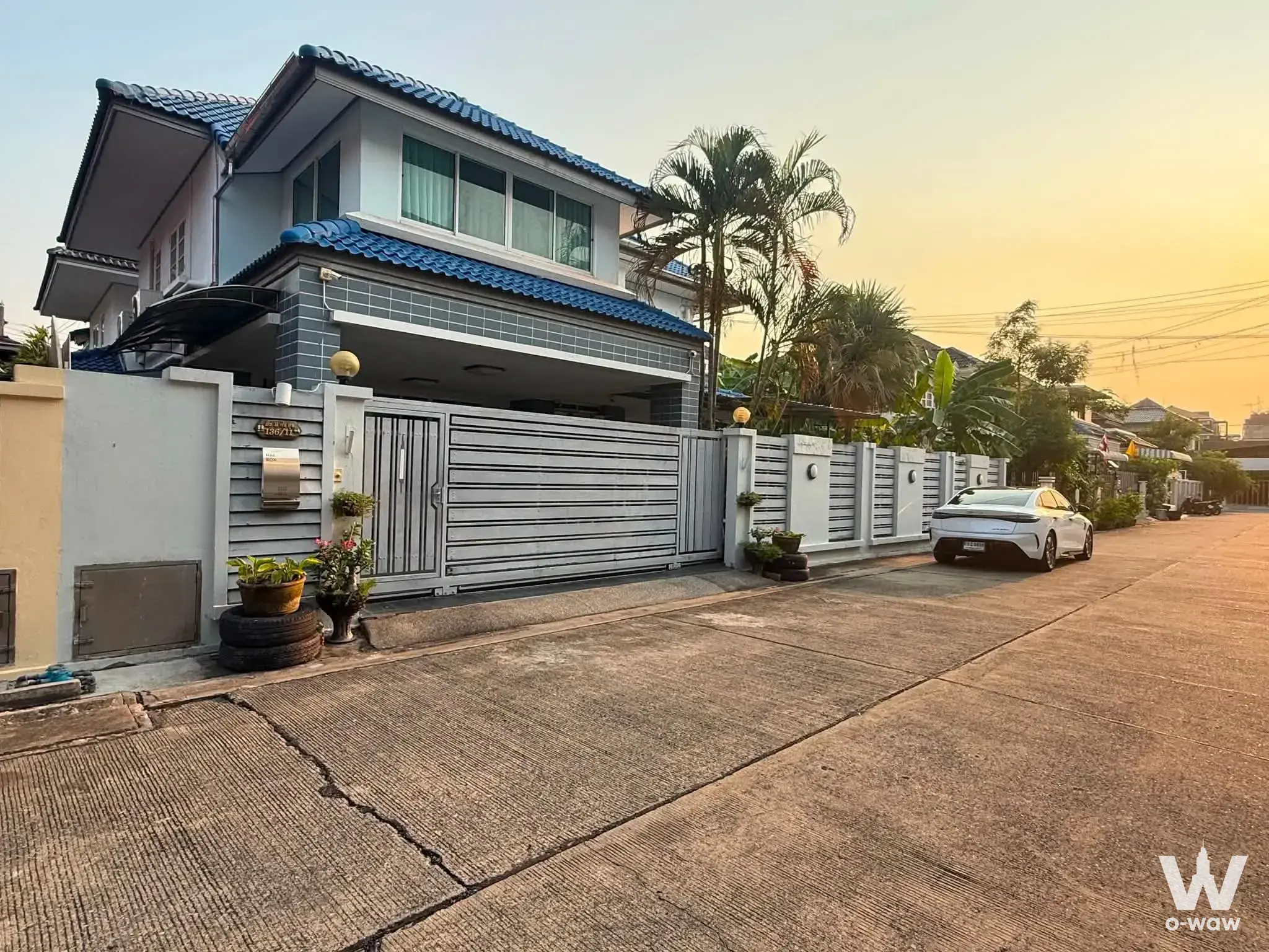 Two-story house for sale at Vino Ratchada 32 featuring blue tile roof, brick facade, and carport at sunset