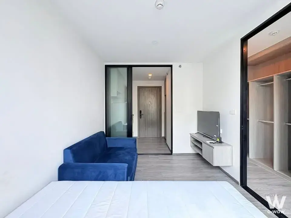 Minimalist studio in The Origin E22 Station with a bare mattress, navy sofa, and floor-to-ceiling mirror reflecting the