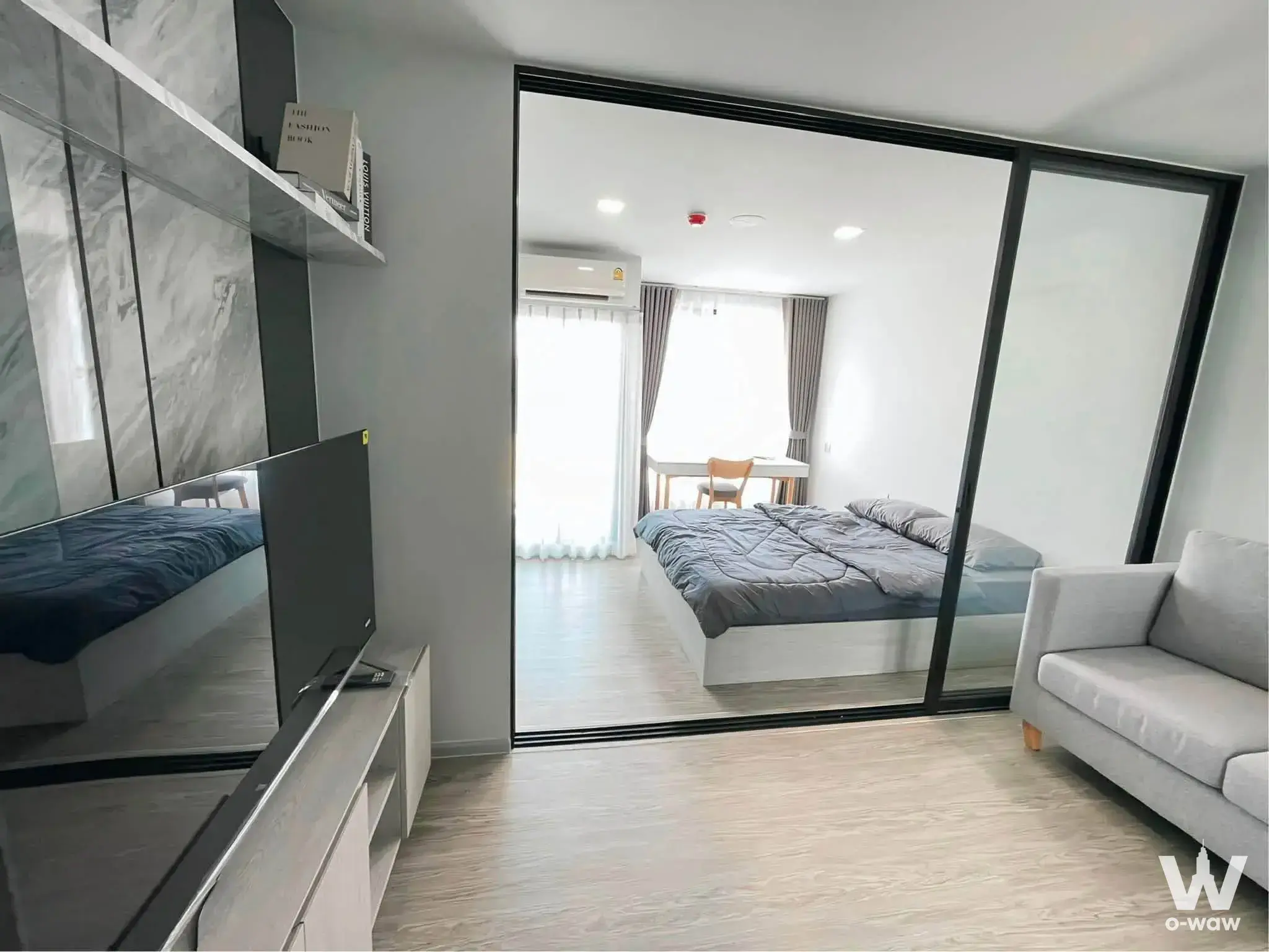 KAVE Seed Kaset studio condo living area with grey marble TV wall, sofa, and glass partition separating the bedroom