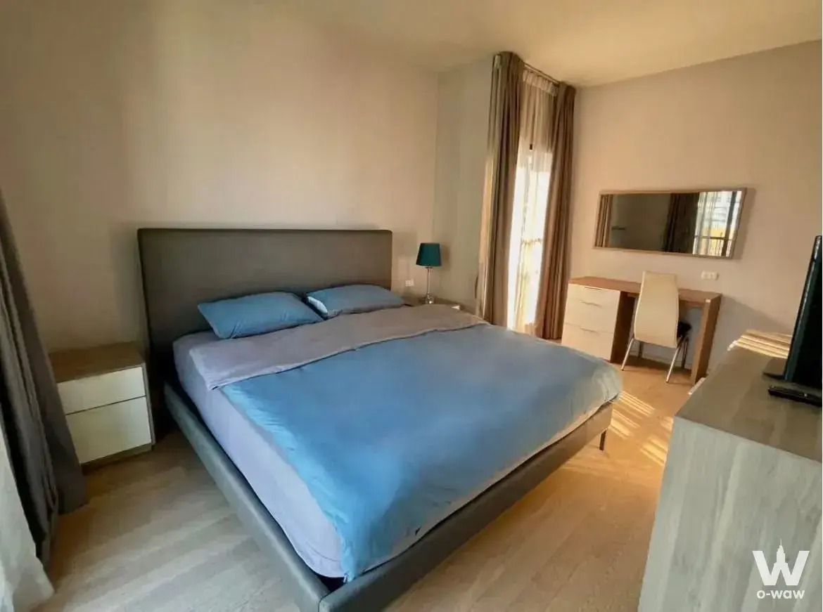 2-bed condo for rent in Noble Refine featuring a modern bedroom with blue accents and natural light