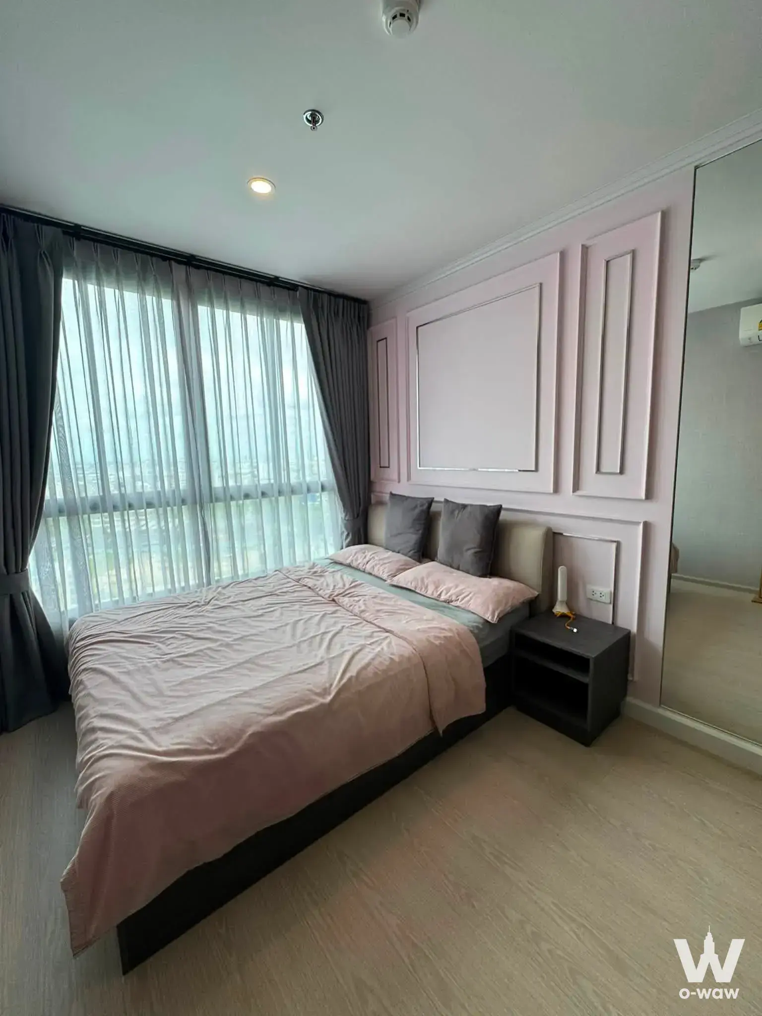 Bedroom in ELIO DEL NEST condo with pink duvet, feature wall panels, and floor-to-ceiling window with city view