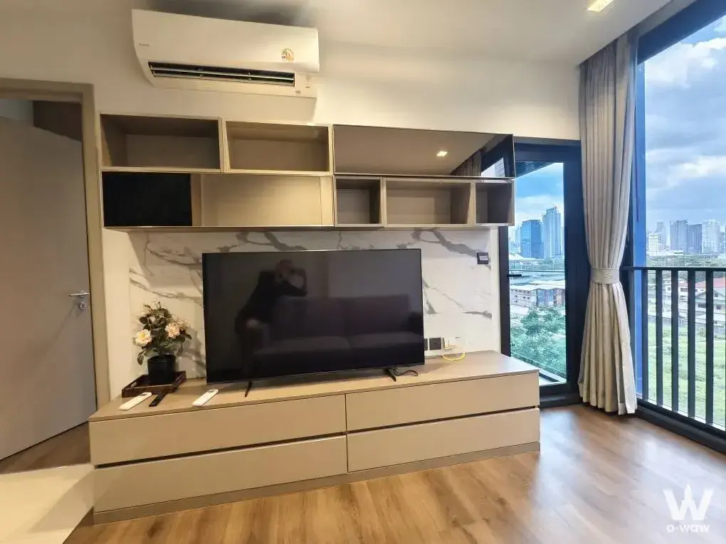 1-bed condo for rent in THE LINE Asoke-Ratchada with living room featuring large TV and balcony city view