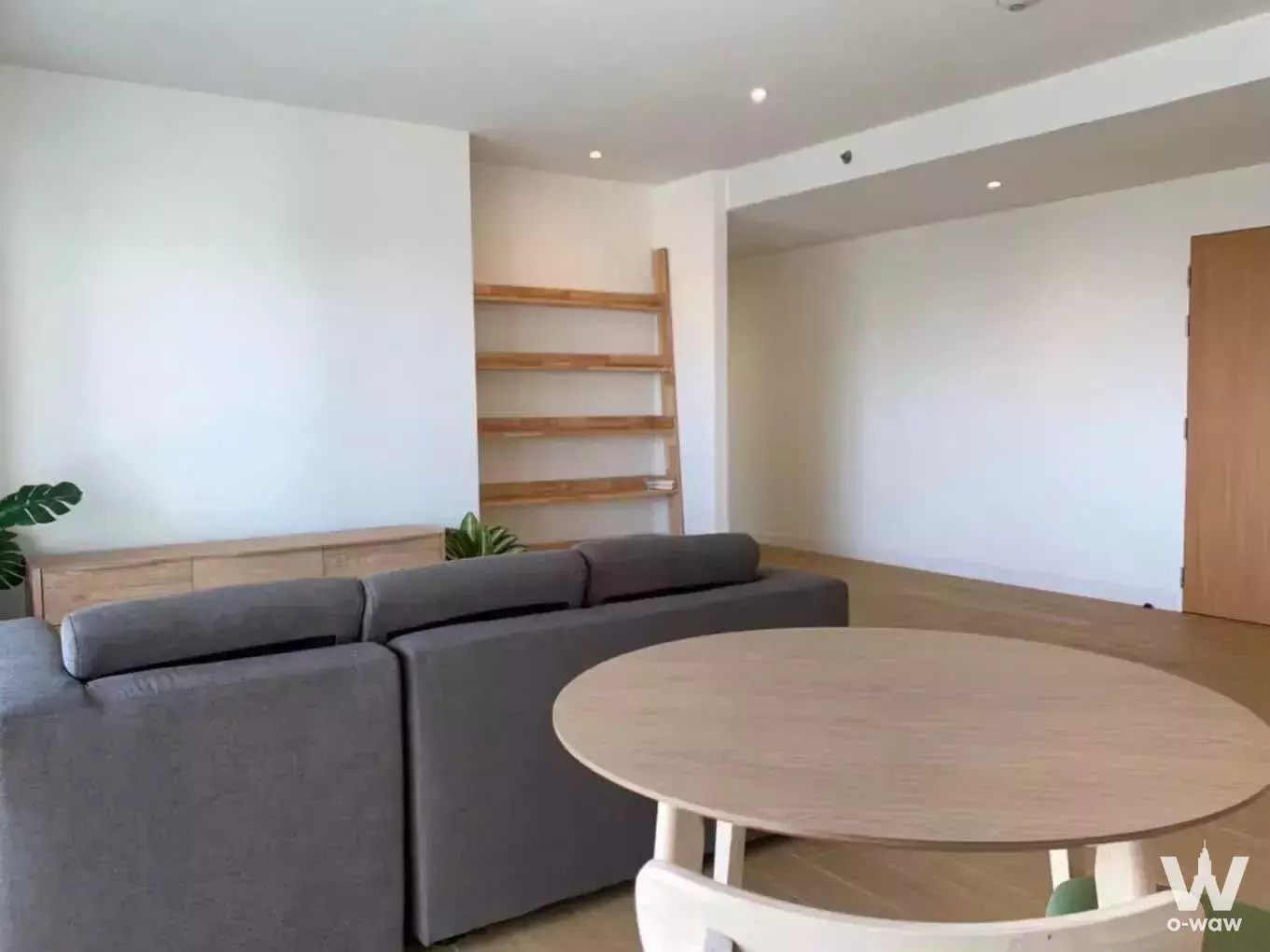 Grey sectional sofa and round wood dining table in the open plan living area of a 2-bed condo for rent