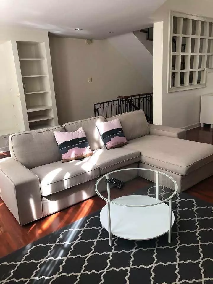 4-bed Baan Klang Krung townhouse living room with beige sectional sofa, hardwood floors, and natural light