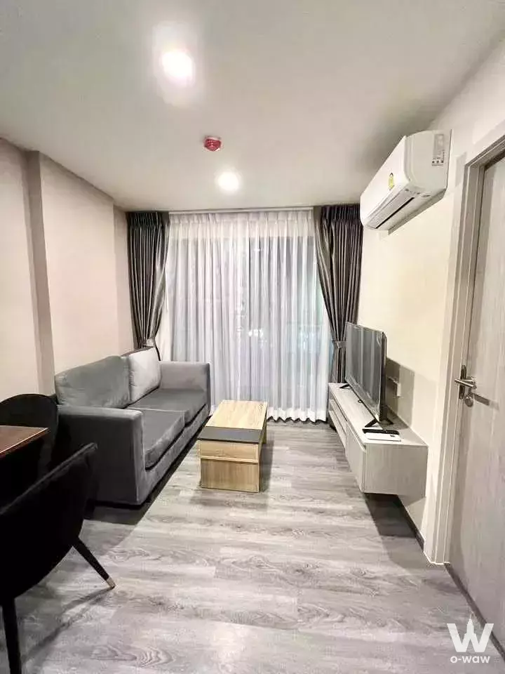 Living room in The Origin Onnut condo with grey sofa, wood coffee table, and sheer curtained balcony door