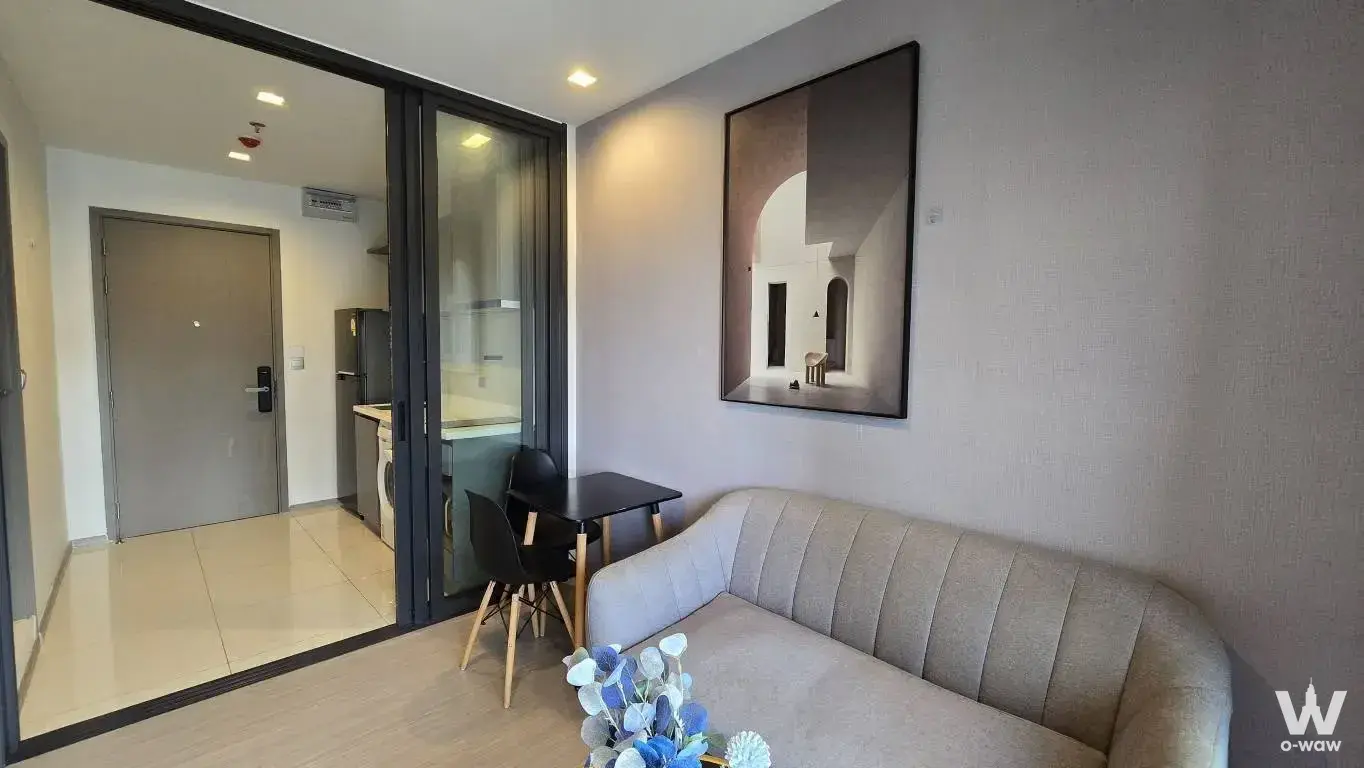 Compact living room in Life Asoke Hype studio with grey ribbed sofa black dining set and framed architectural artwork
