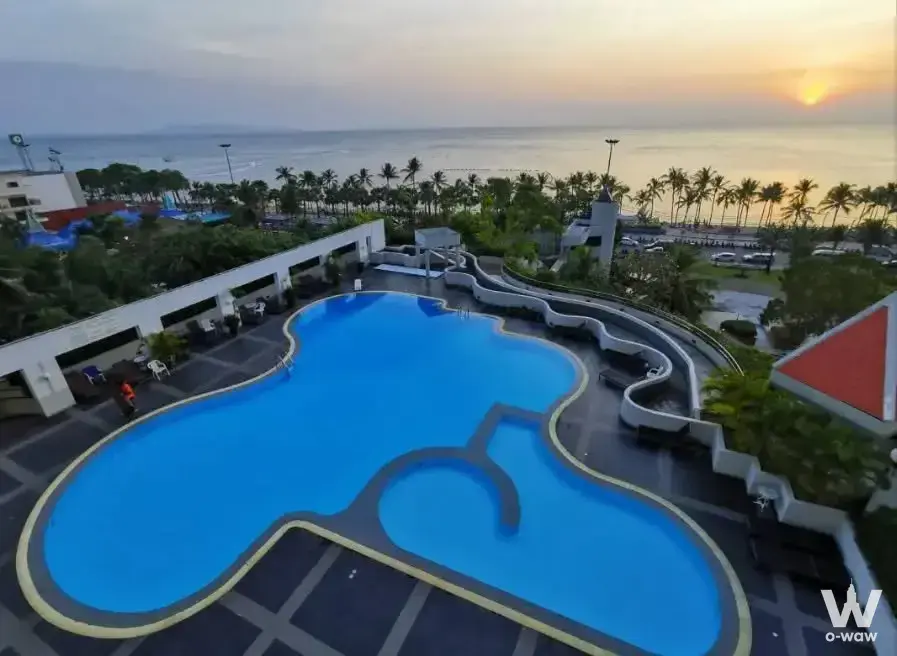 Rooftop pool deck with blue water and lounge chairs overlooking sunset ocean view at Jomtien Plaza Condotel