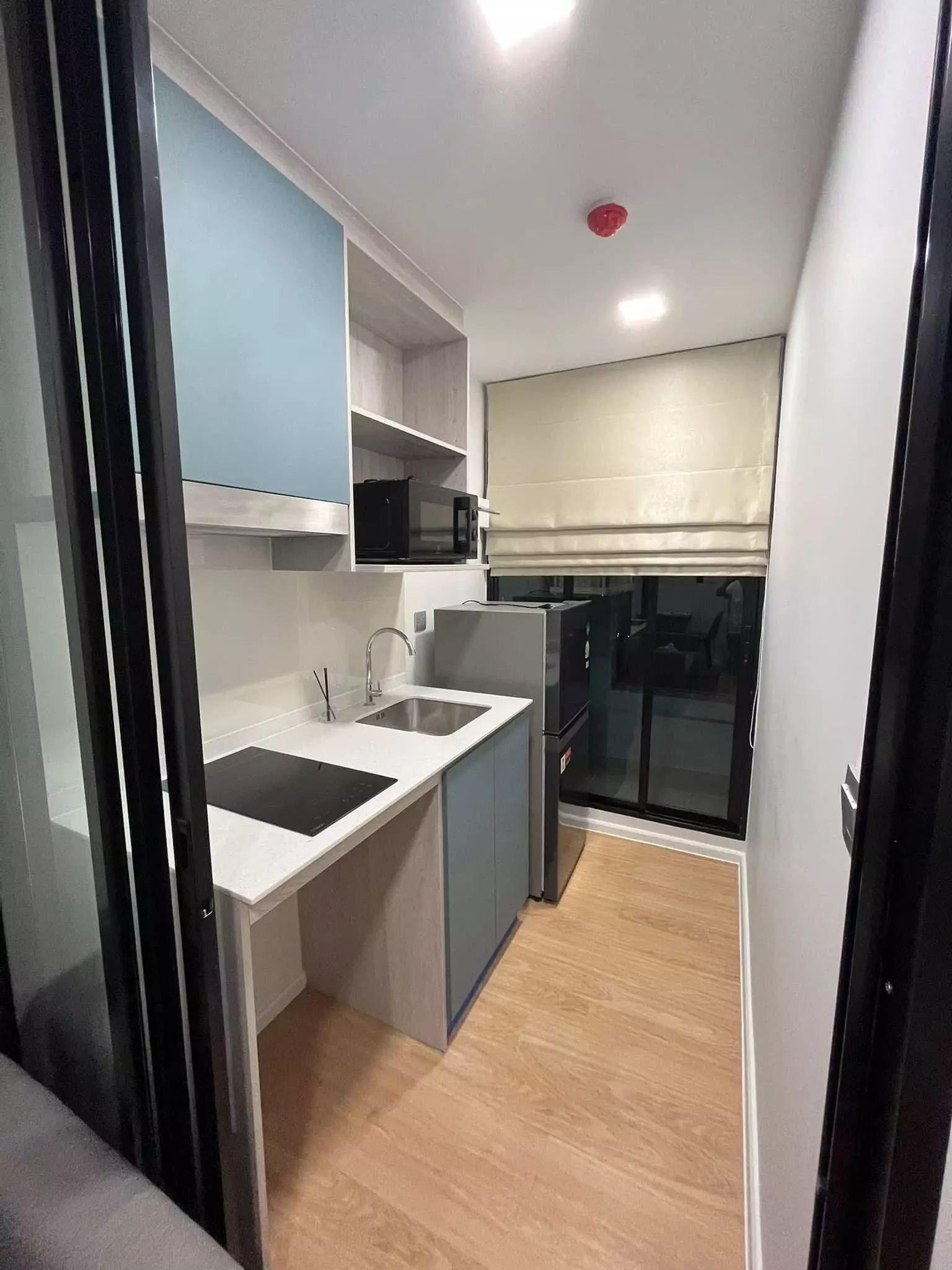 Compact galley kitchen in a 1-bed Atmoz Kanaal Rangsit condo with blue cabinets and induction cooktop