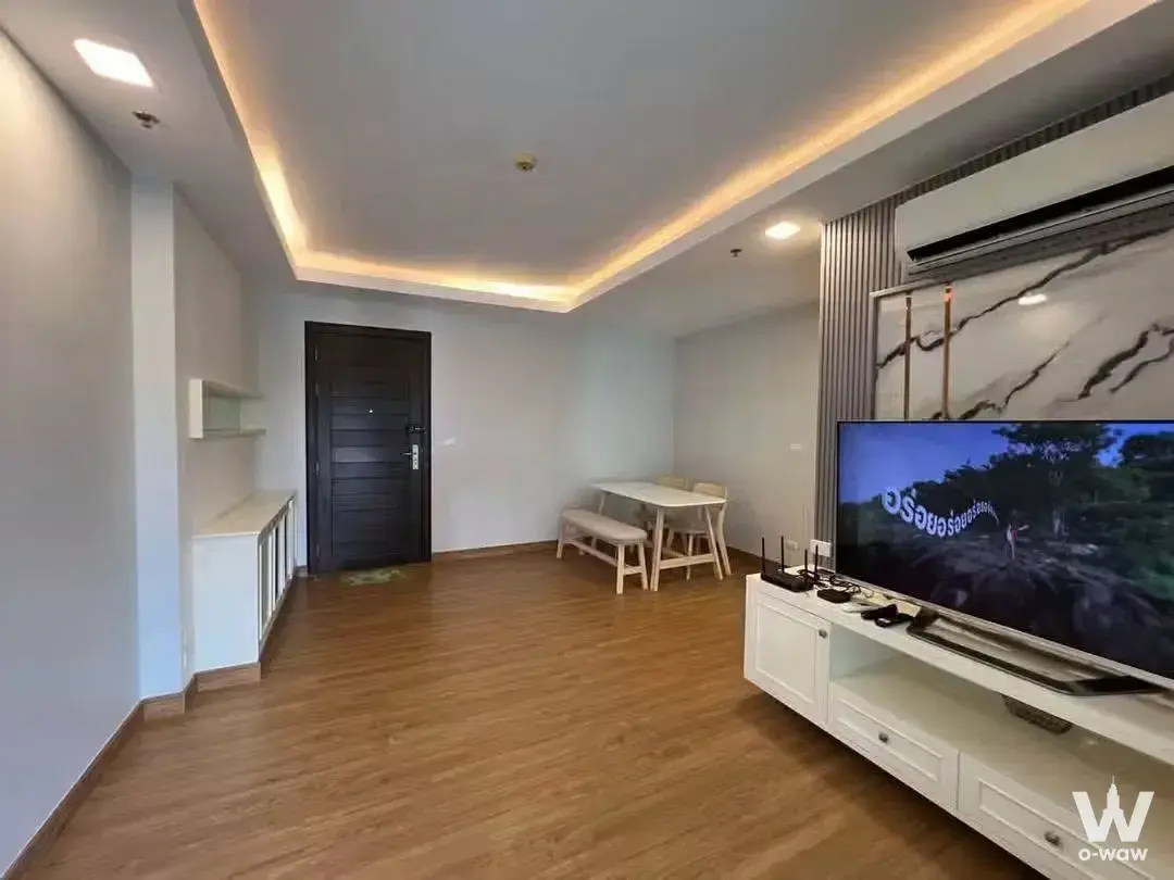 Open-plan living area in Thru Thong Lor condo for sale with marble feature wall, LED cove lighting, and wood tones