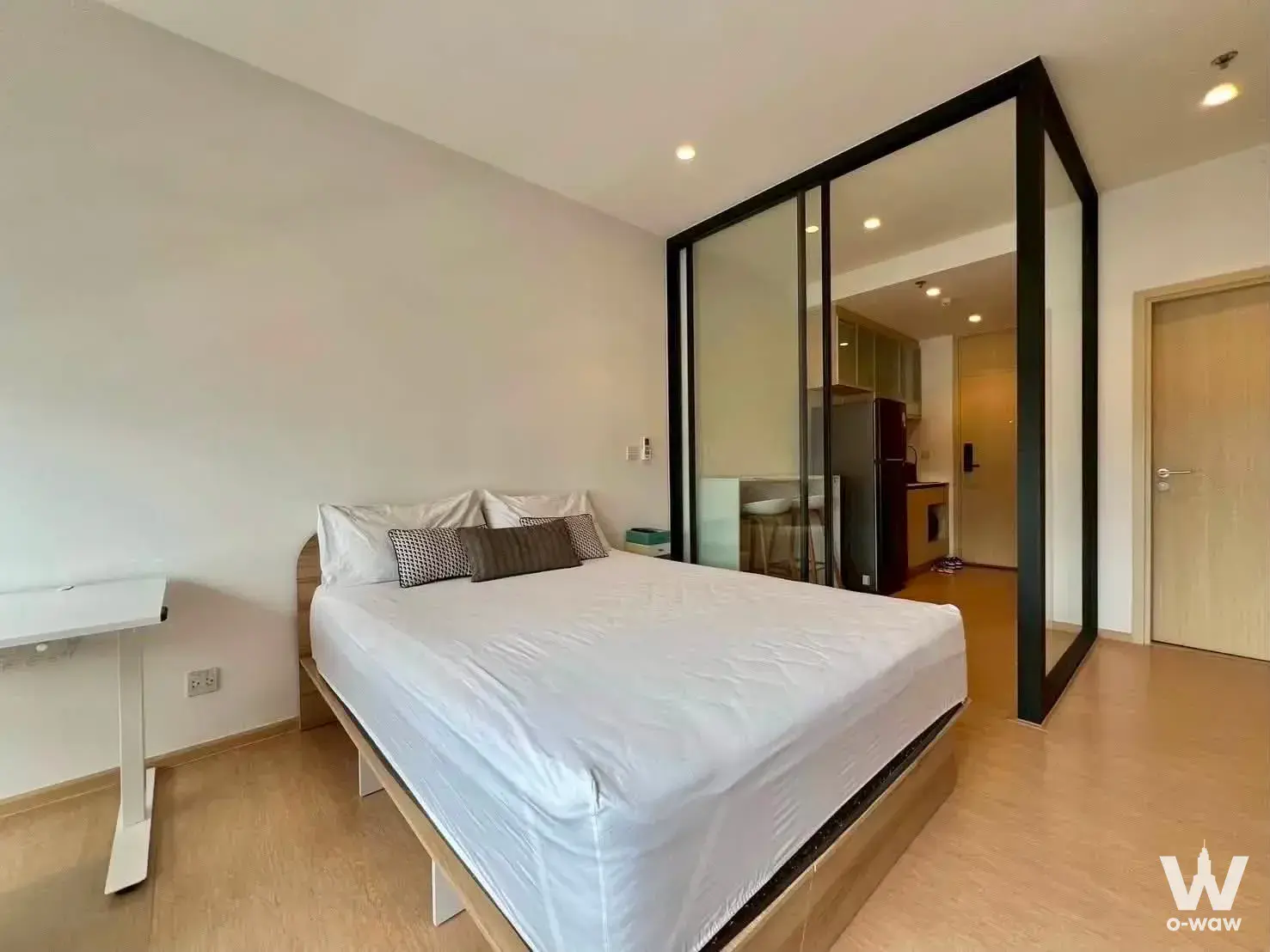 Modern bedroom in MARU Ekkamai 2 condo with glass partition revealing kitchen and light oak flooring