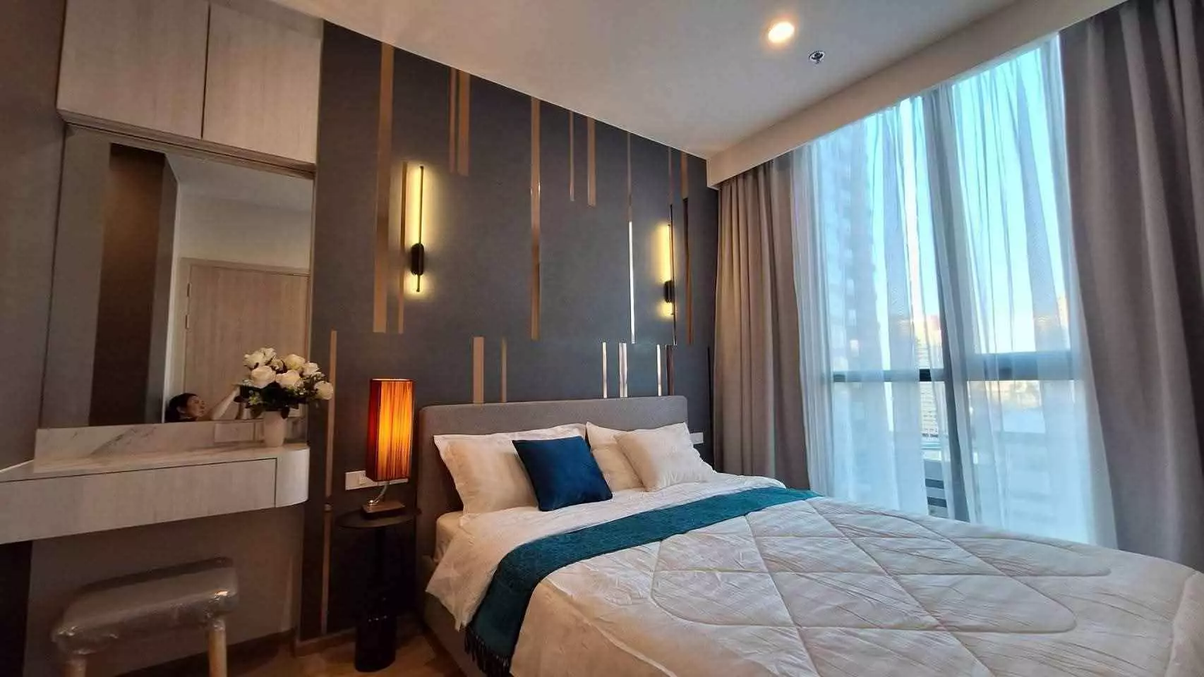 Grey upholstered queen bed against a gold-accented wall with floor-to-ceiling city views in Nue District R9