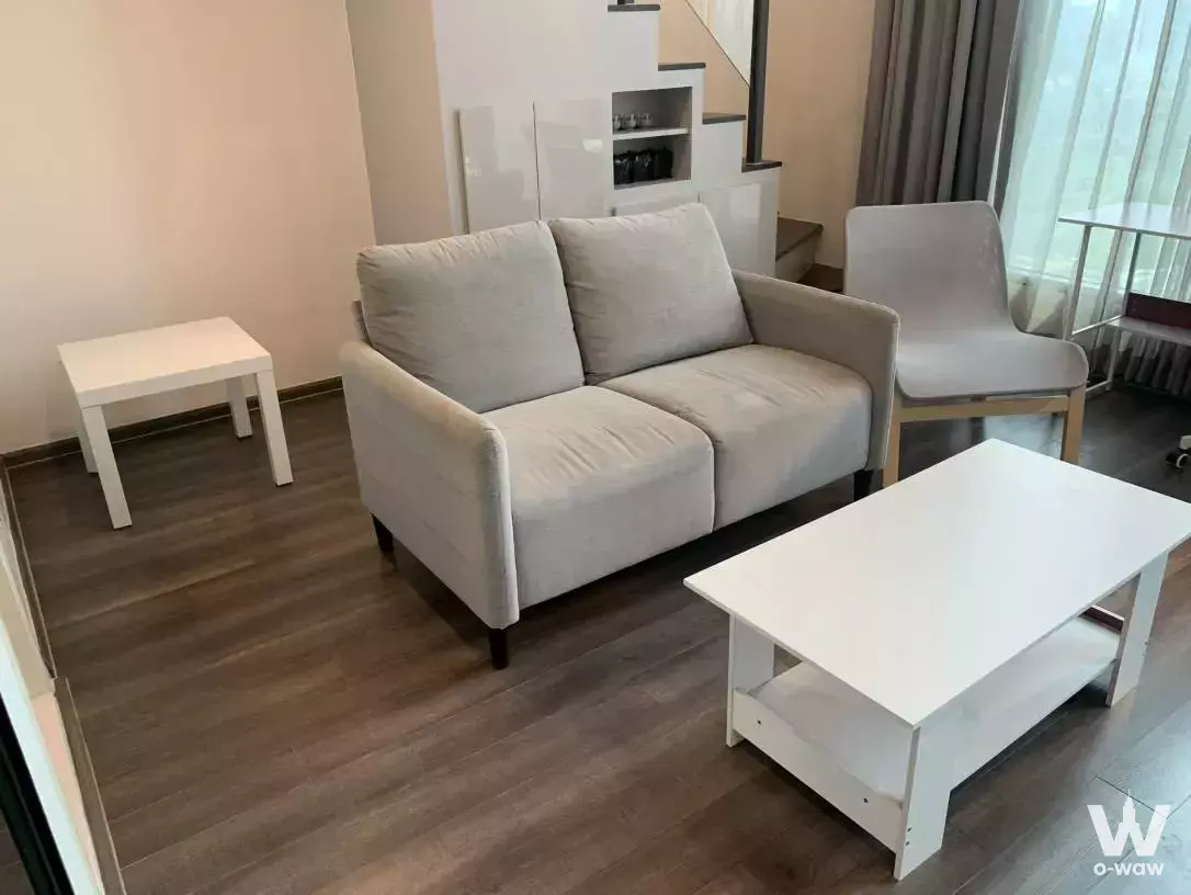 Bright living room in KnightsBridge Space Rama 9 condo with grey sofa, white coffee table, and floor-to-ceiling windows