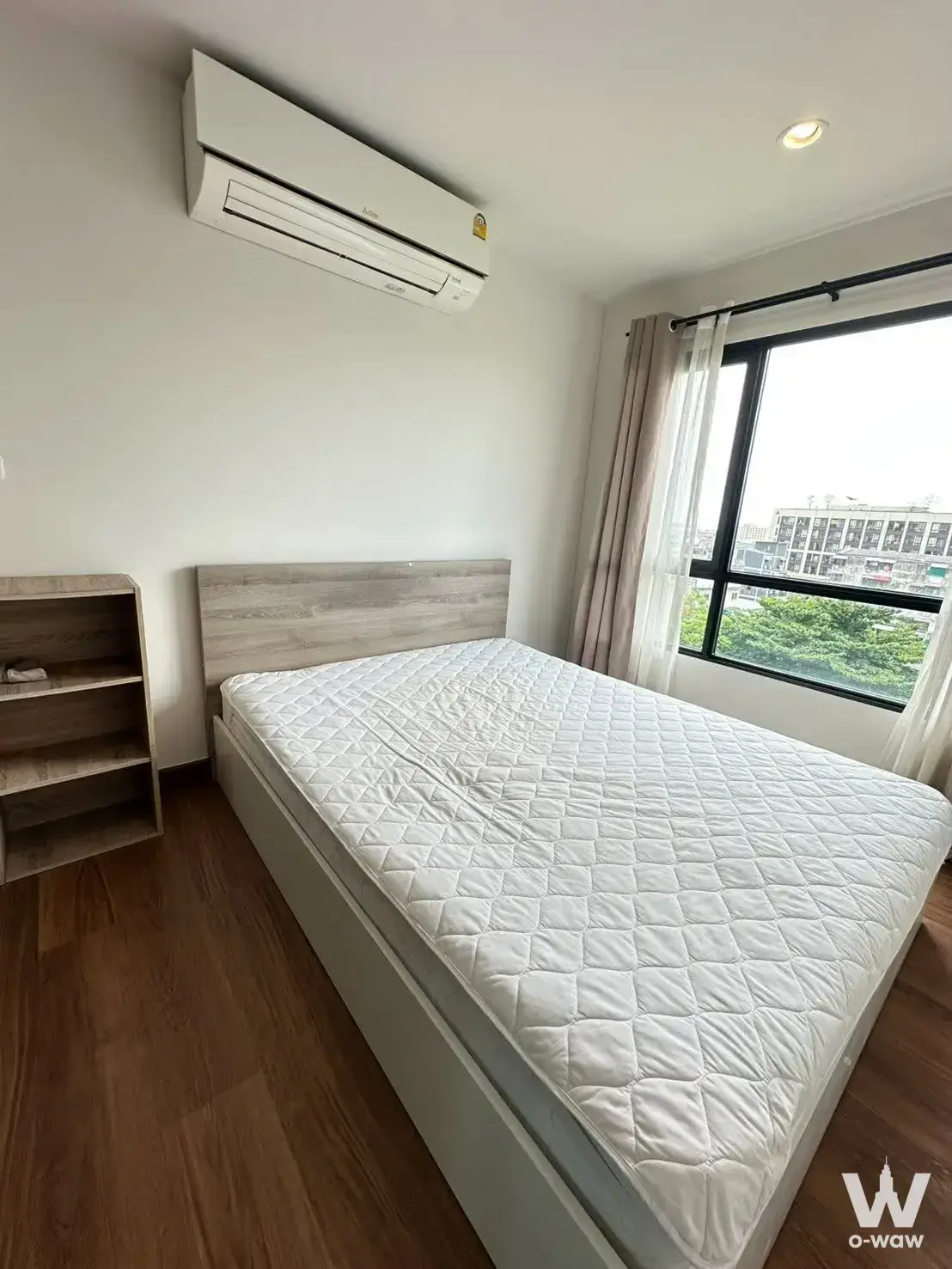 Minimalist bedroom in a Phahonyothin condo with a white bed, wood headboard, and city window view