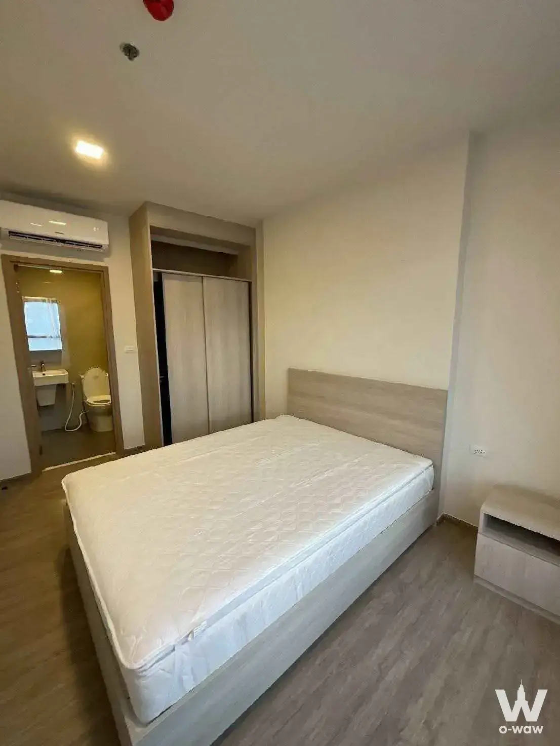 Bedroom in NIA by Sansiri with a light wood queen bed frame and an open doorway leading to the en-suite bathroom