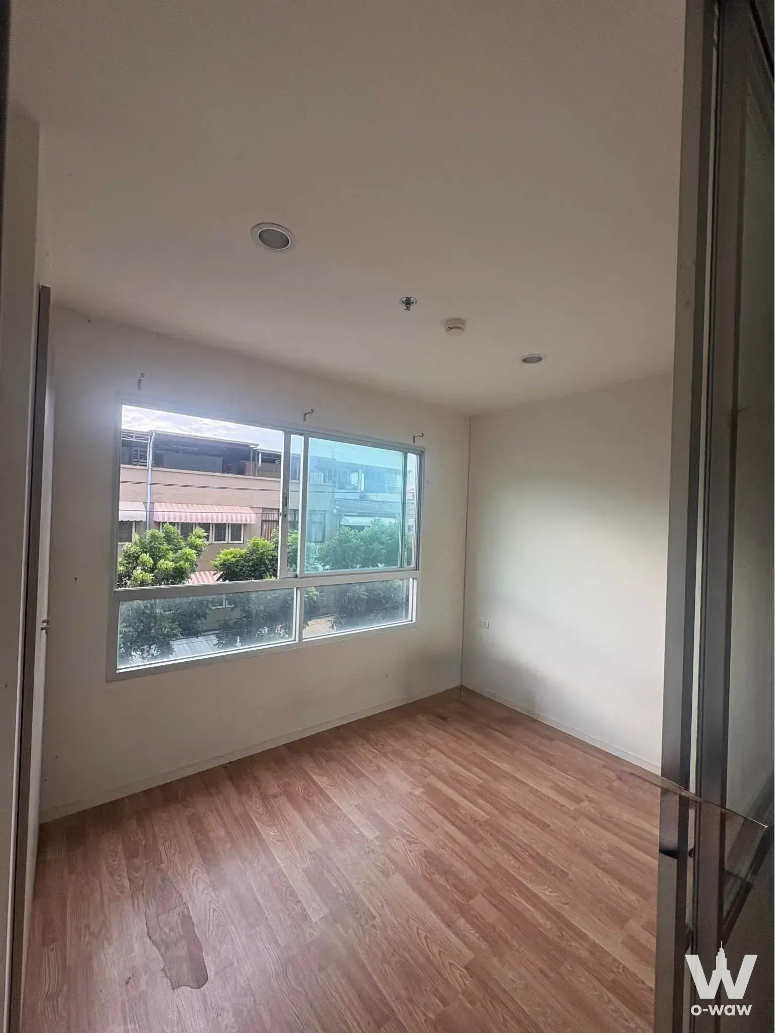 Empty room in Lumpini Park Nawamin condo featuring light wood floors and sliding window with street view