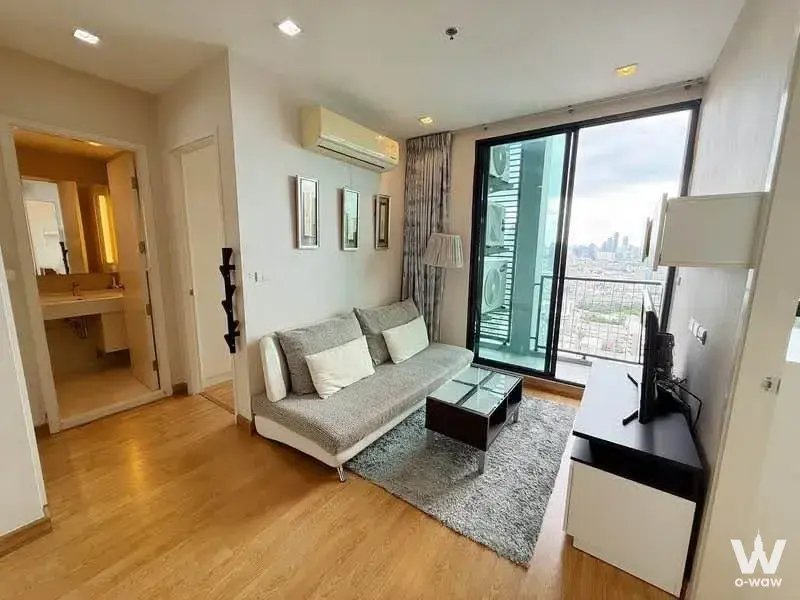 Furnished living room in Q House Sukhumvit 79 condo with grey sofa and balcony access