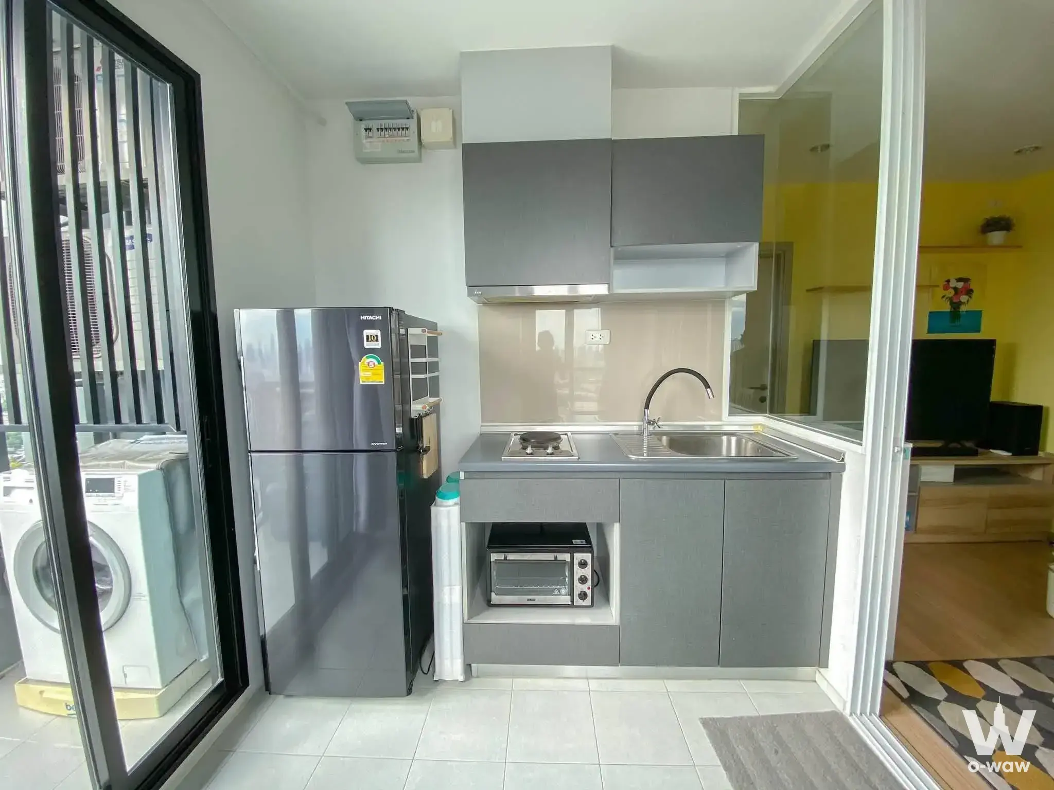 Kitchen in THE BASE Rama 9 condo with dark cabinets and glass door to service balcony