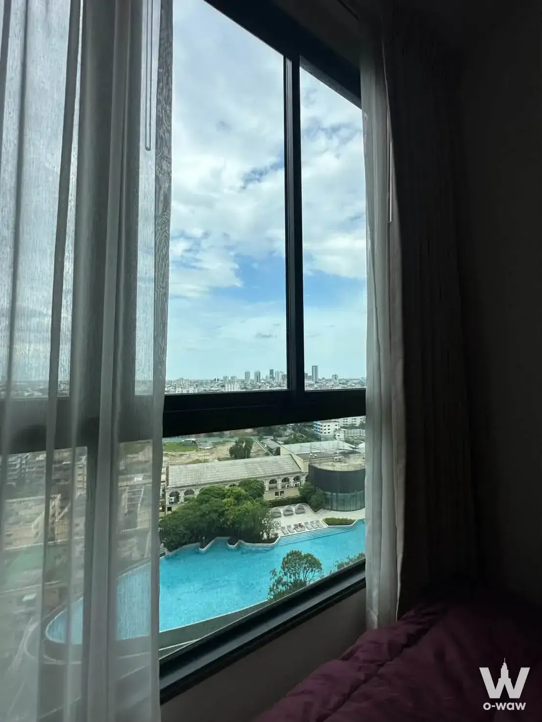 Bedroom in ELIO DEL NEST with large window overlooking a bright blue swimming pool and city skyline