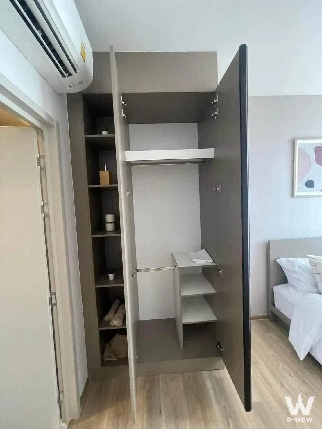 Open dark-grey wardrobe with organized storage in a furnished Oka Haus bedroom with light wood floors
