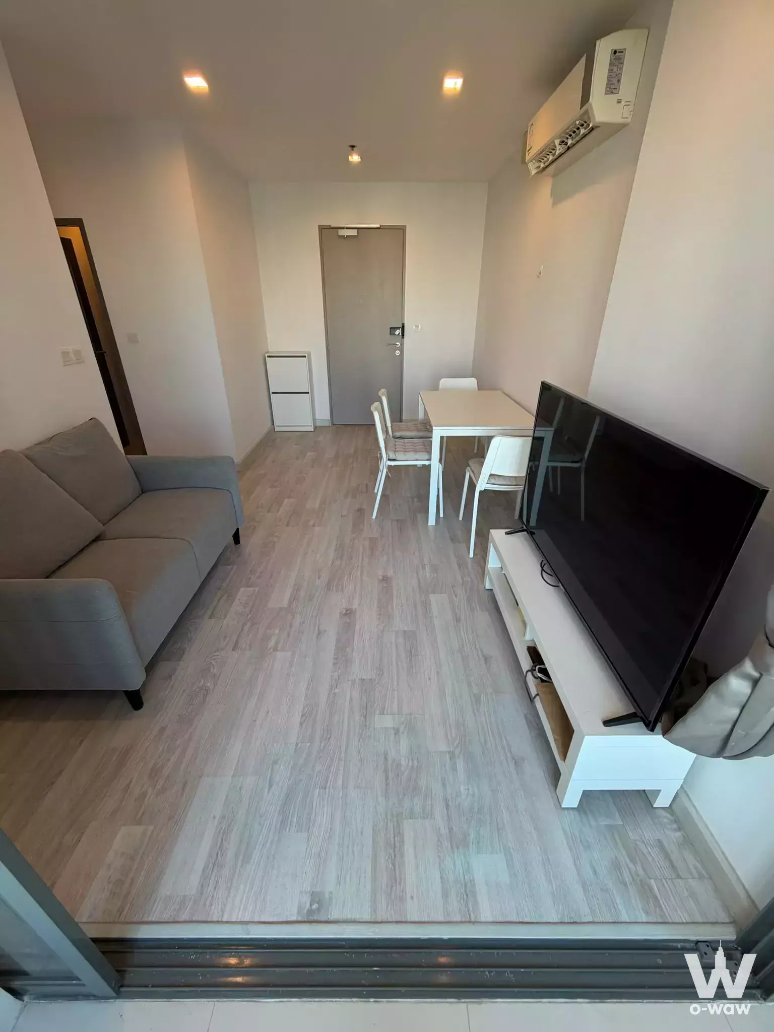 Living area in Ideo Mobi Sukhumvit 81 with grey sofa, white dining set, and light wood laminate floors