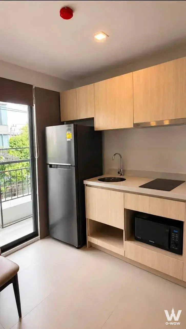 Compact kitchenette with induction cooktop and balcony access in The Nest Sukhumvit 64 rental