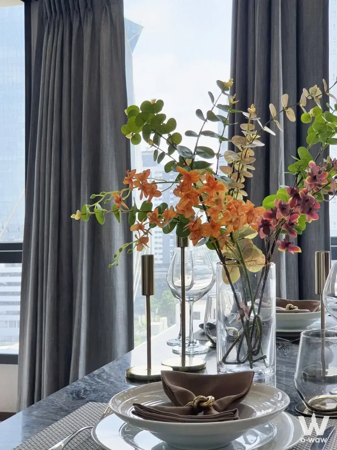 Formal dining setup on a dark marble table with orchids and city views in this 1-bed CONNER Ratchathewi condo