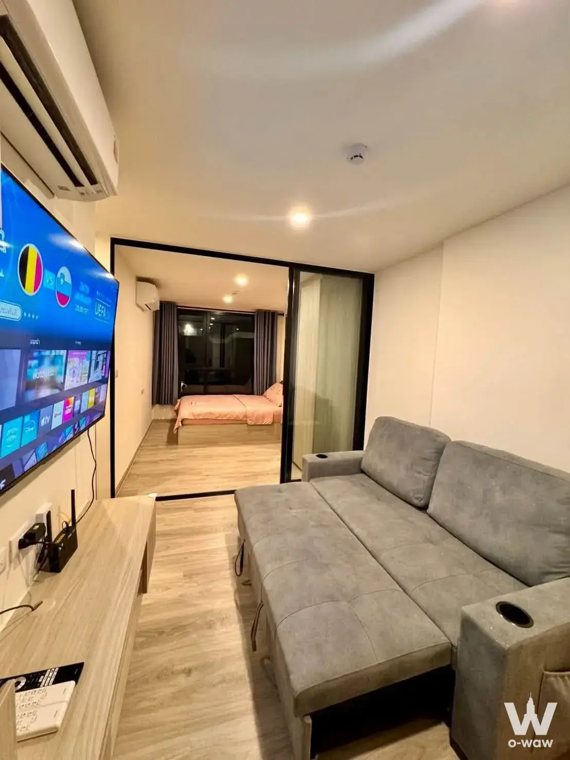 Living room in Origin Play Sri Udom Station studio condo with grey sofa and wall-mounted TV