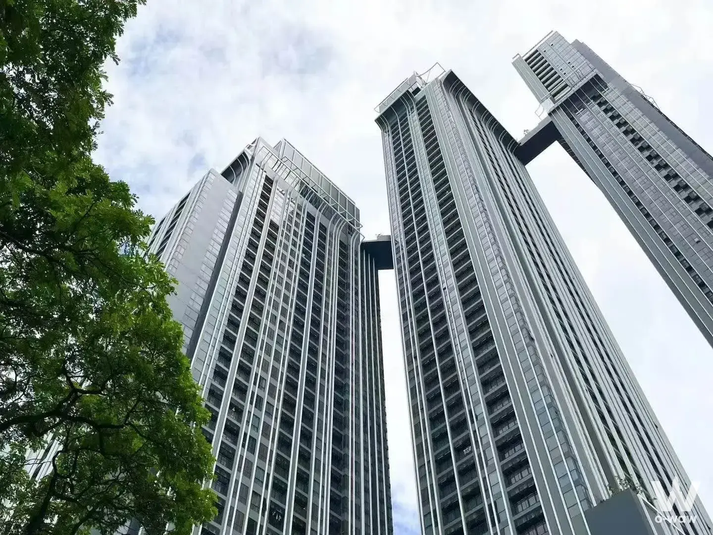 Modern exterior of Park Origin Thonglor with silver towers and skybridge under an overcast sky