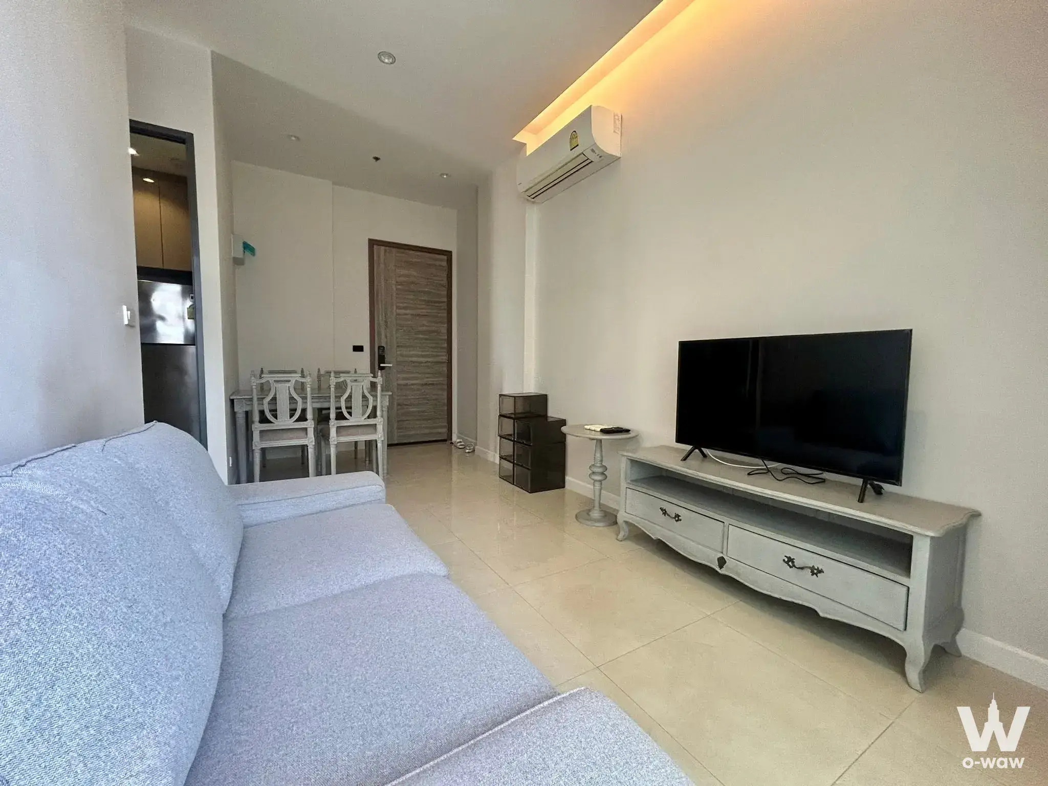 Open-plan living area in Mayfair Place Sukhumvit 50 with a light-blue sofa and distressed white console