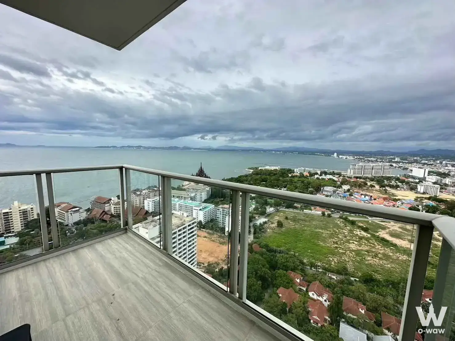 This high-floor balcony in a 1-bed condo rental at The Riviera Wongamat Beach has a glass railing and a panoramic sea view