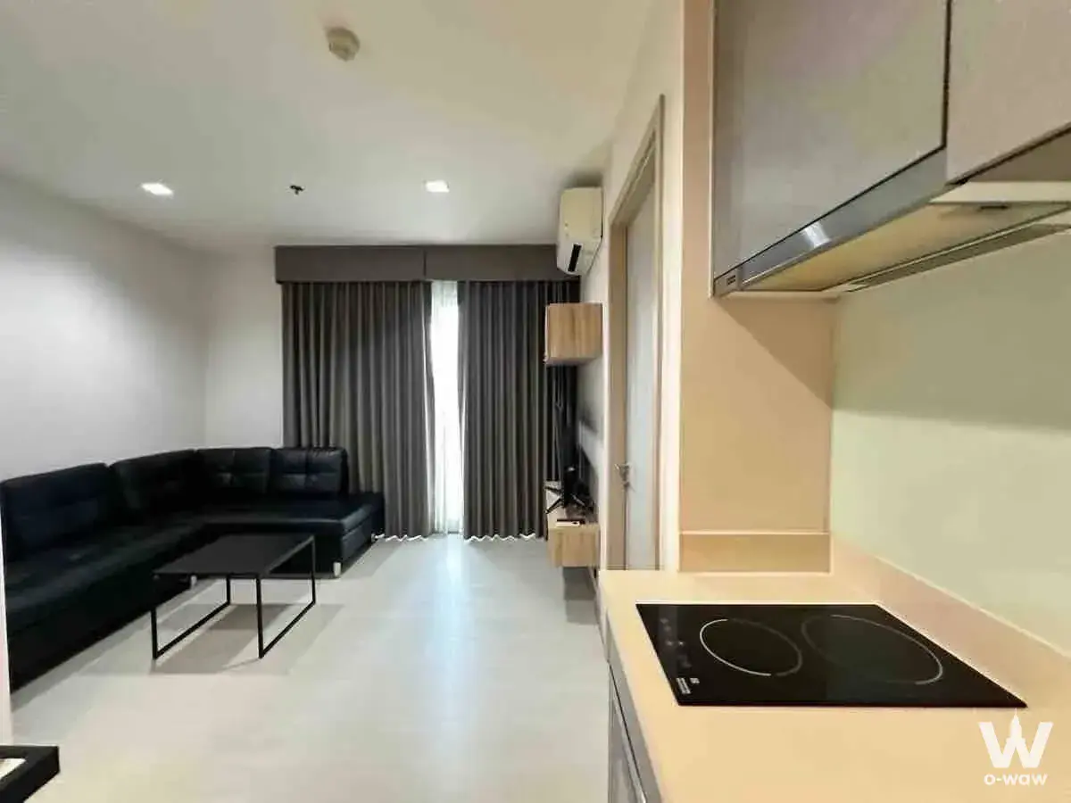 Open-plan kitchen and living room in Rhythm Sukhumvit 36-38 with black leather sofa and cooktop