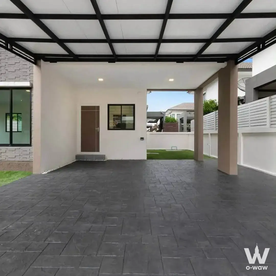 The covered carport of a 3-bed Bang Yai house for sale has grey pavers, a white ceiling and a brown door