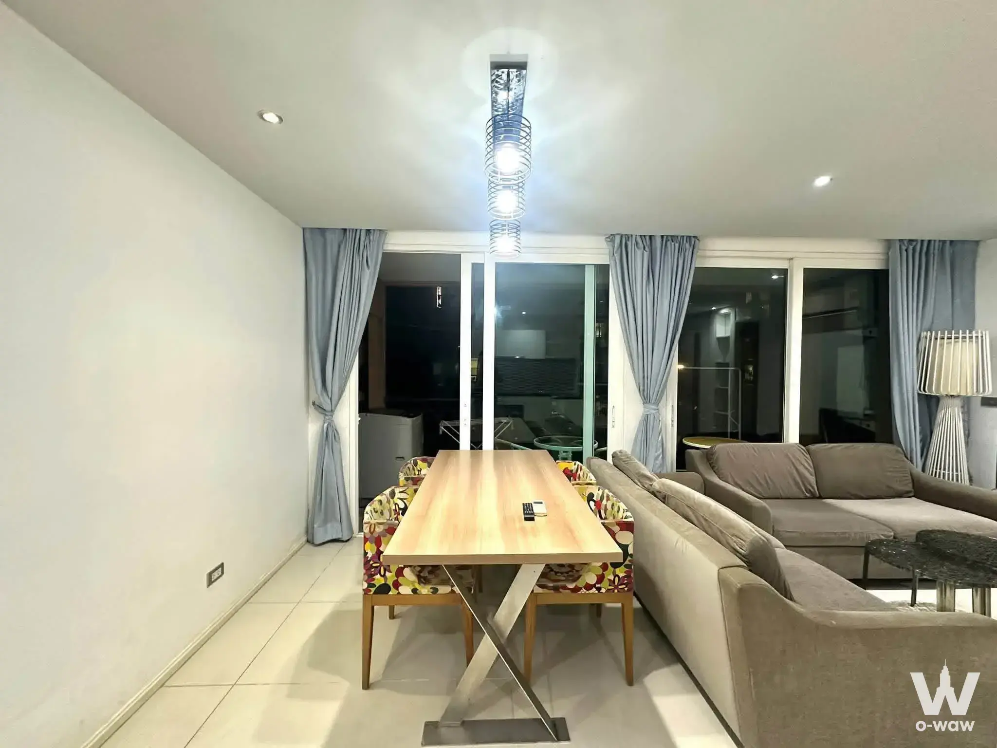 This open-plan living and dining area in a 2-bed condo rental in Atlantis Condo Resort Pattaya has a grey sofa and balcony