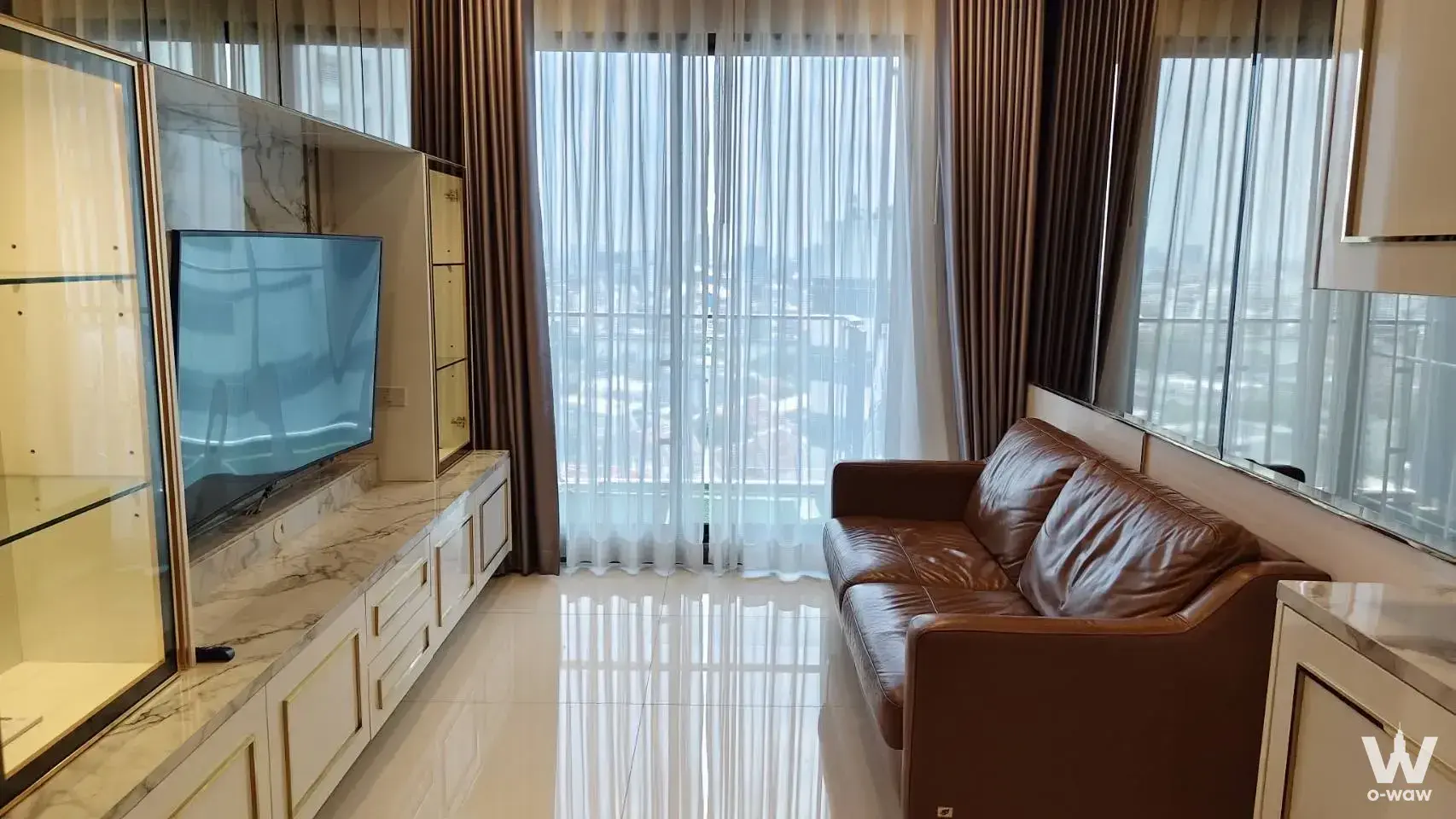 Supalai Premier Charoen Nakhon living room with brown leather sofa, marble TV panel, and city view