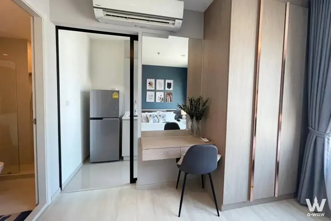 Life Asoke 1-bed condo desk nook with floating wood desk, wardrobe, and glimpse of bathroom and kitchenette