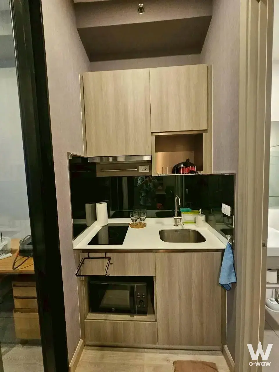 Compact kitchenette in KnightsBridge Prime Onnut with light wood cabinets and black induction cooktop