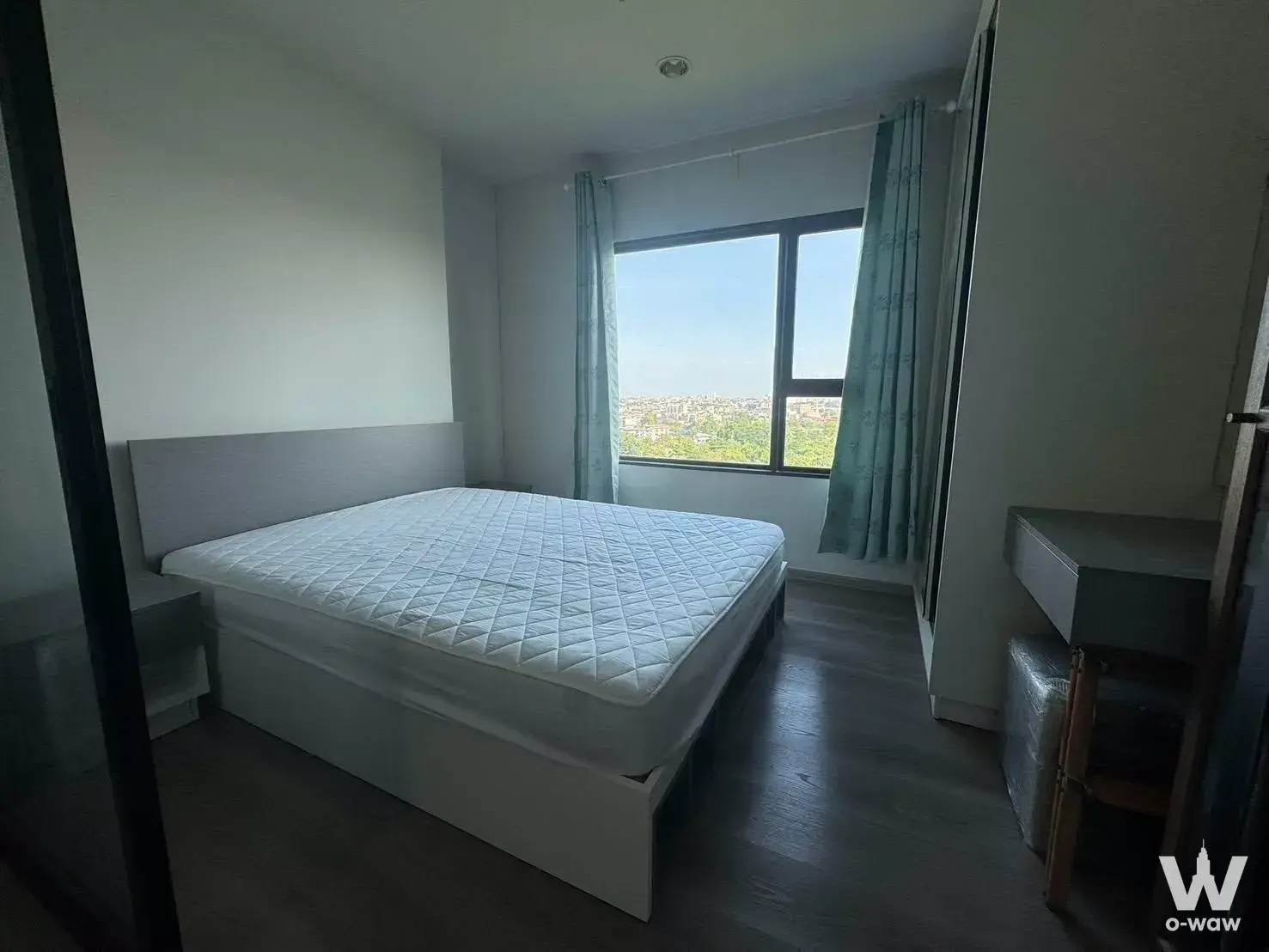 Bright bedroom in a 0-bed condo for sale at Aspire Sathorn-Taksin has a white bed and large window with skyline view