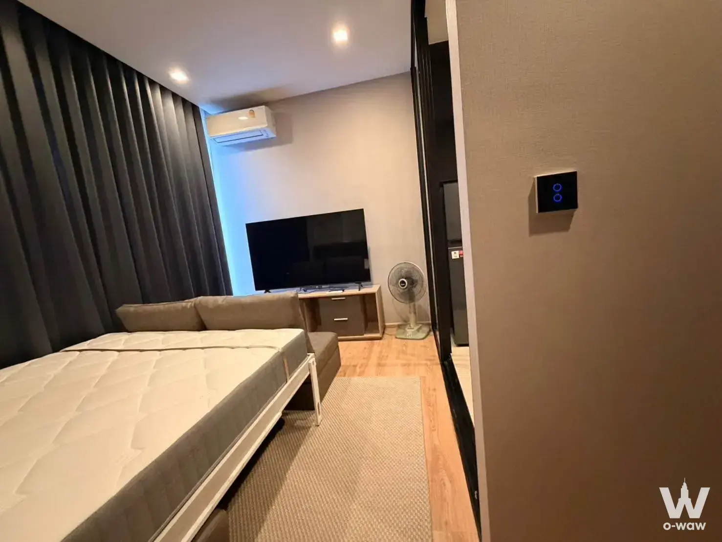 Studio bedroom in Noble Around Ari condo featuring queen bed, TV stand, and neutral tones