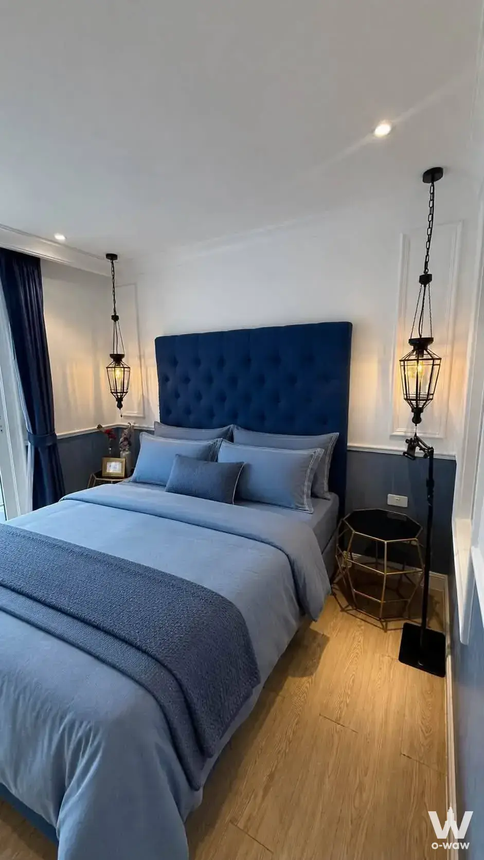 Modern bedroom in a 1-bed condo for sale at Seven Seas Côte d'Azur featuring a navy velvet headboard and industrial pendant