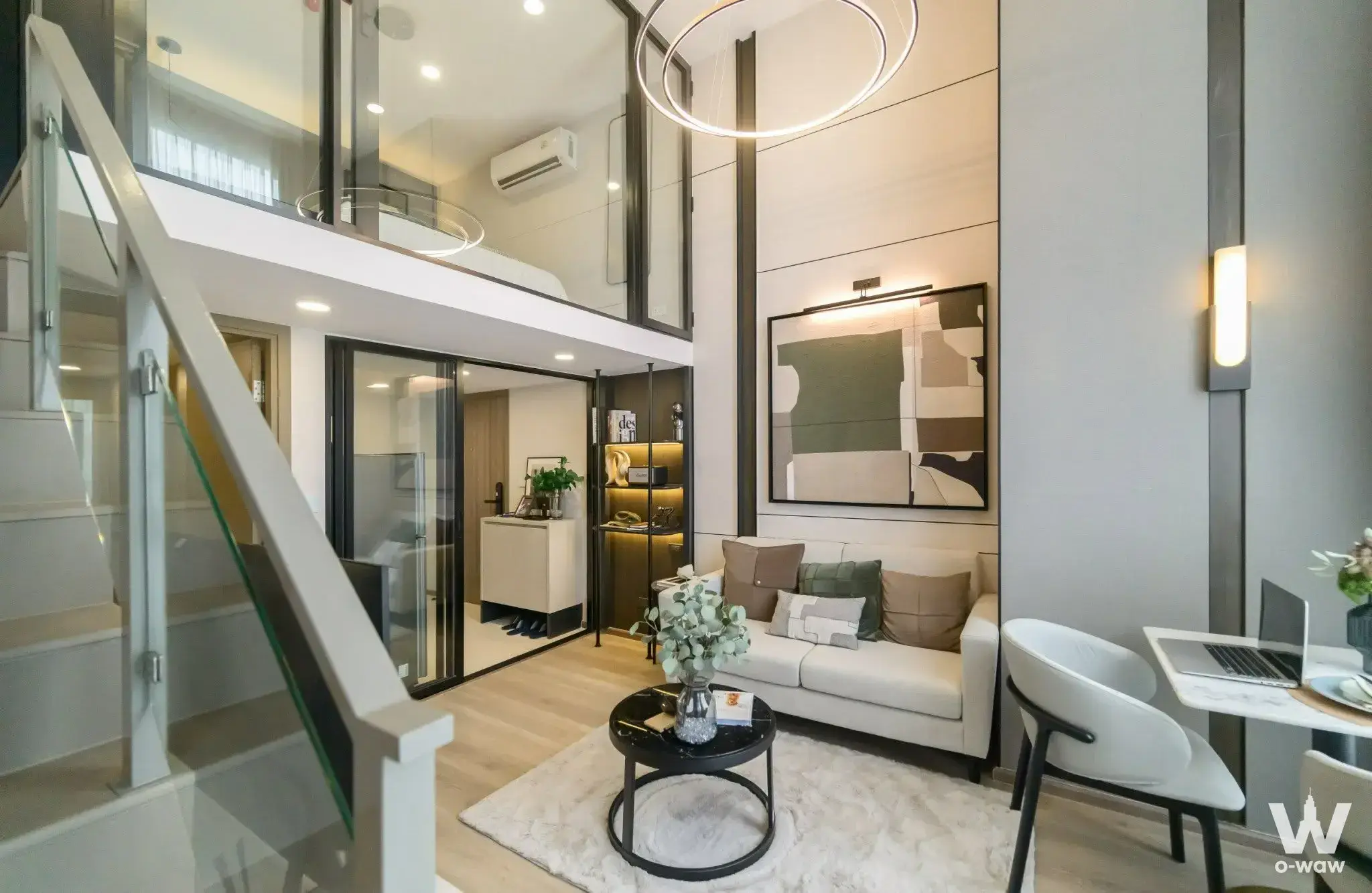 Loft living room in a 1-bed KnightsBridge Space condo with double-height ceiling, sofa and glass-railed staircase