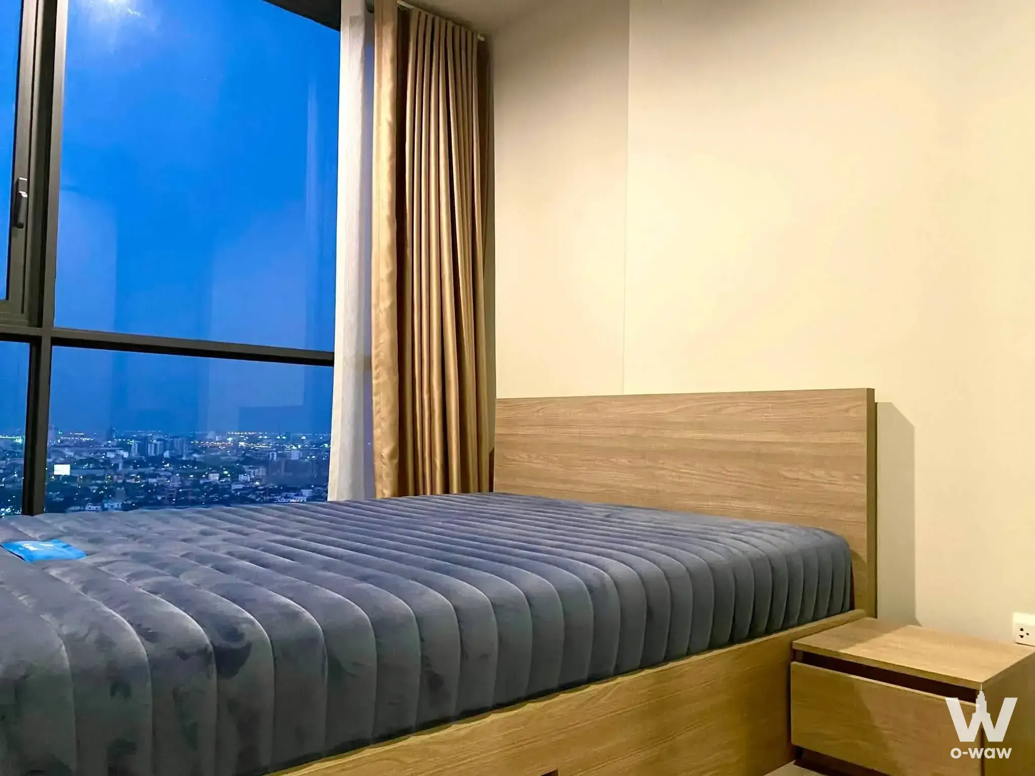 1-bed condo for sale in THE LINE Wongsawang featuring light-wood platform bed and dusk city skyline view